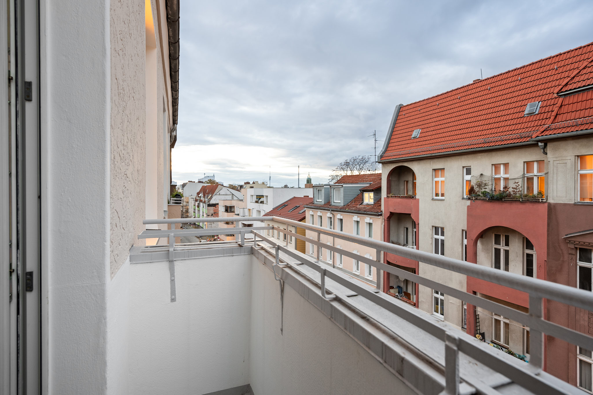 Balkonaussicht auf eine ruhige Wohnstraße mit Altbauhäusern und roten Ziegeldächern bei Abendlicht.