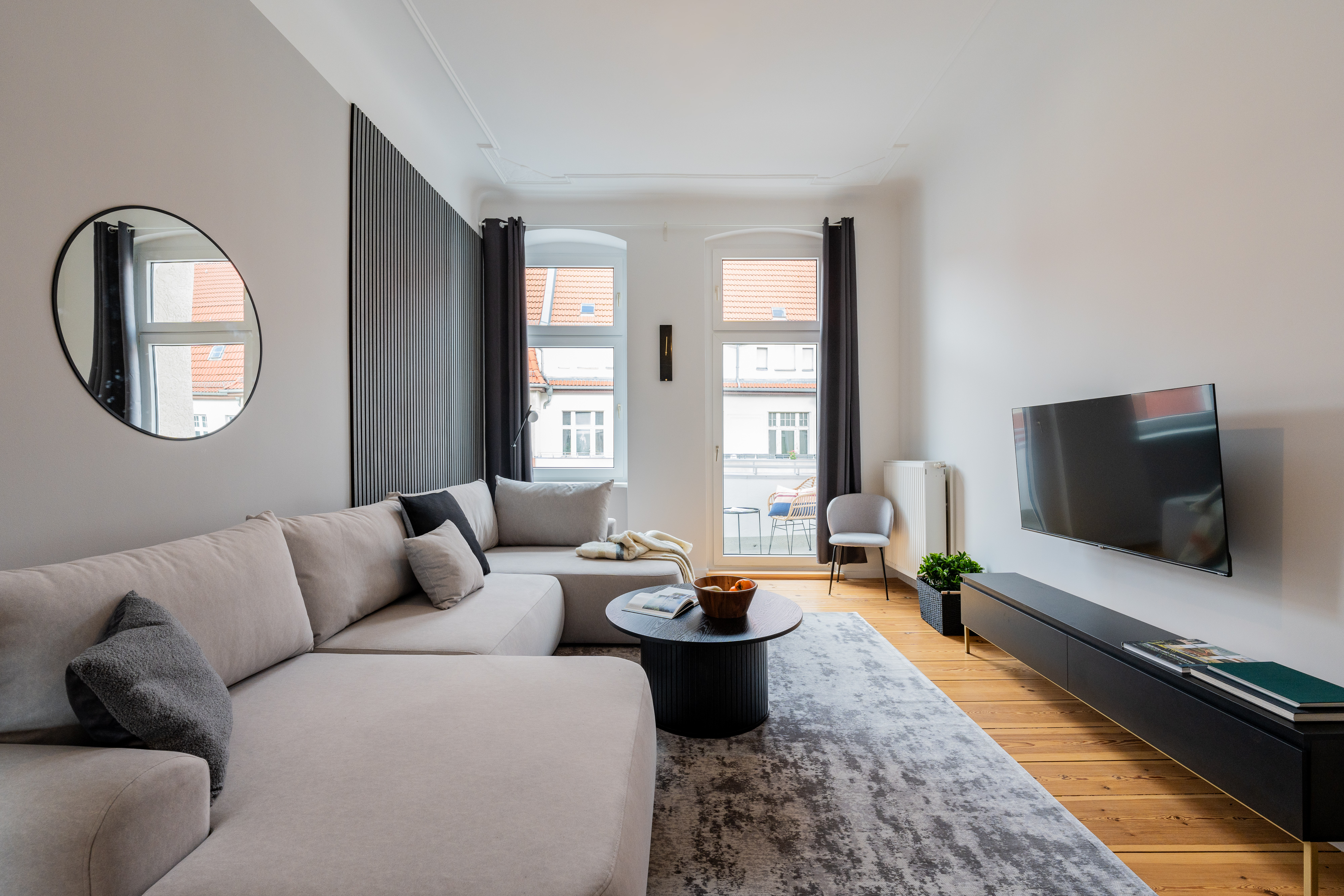Modern living room in a period building with light corner sofa, round coffee table, hardwood floors and balcony access