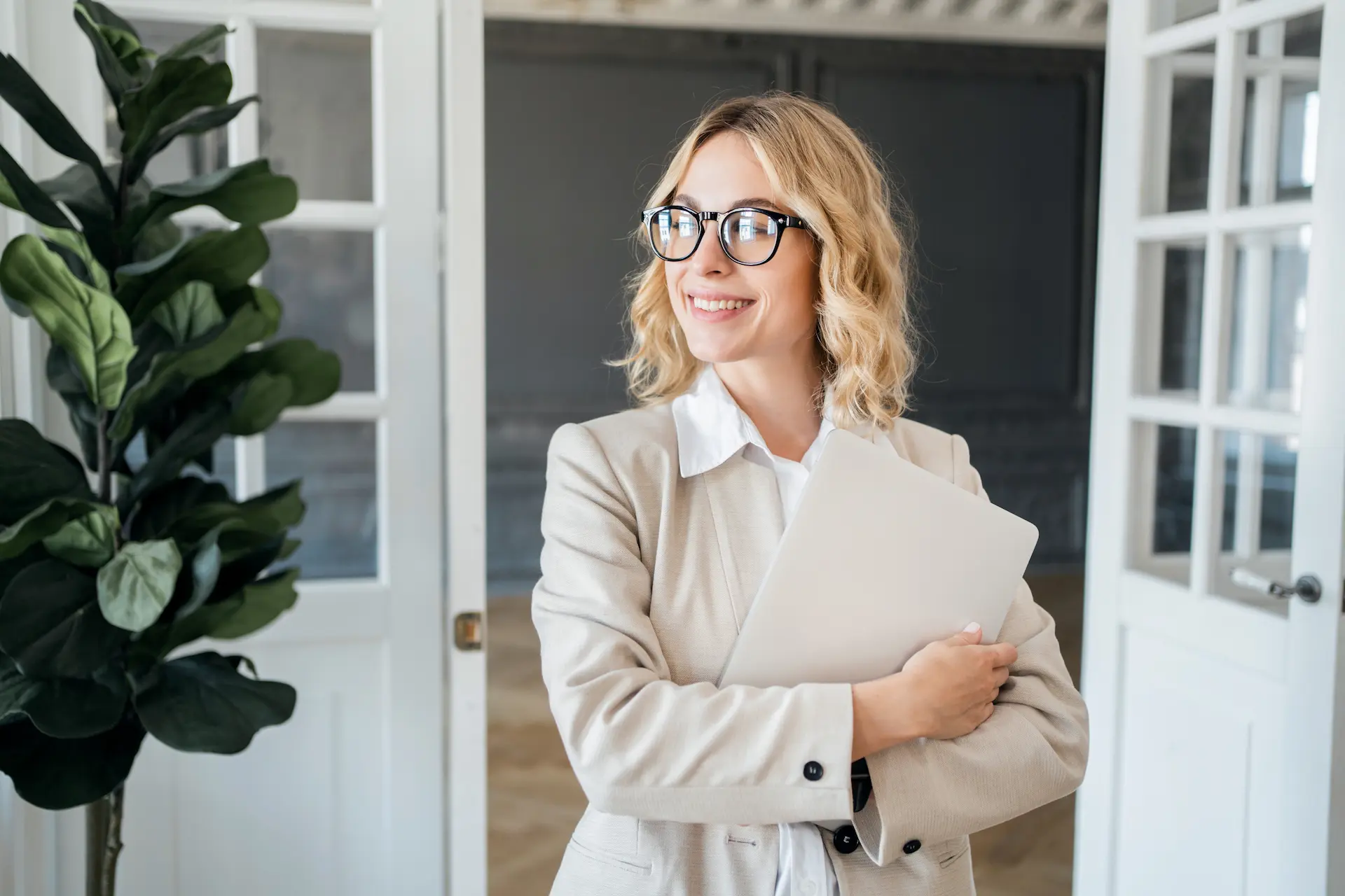 Smiling businesswoman holding a laptop in a modern office.