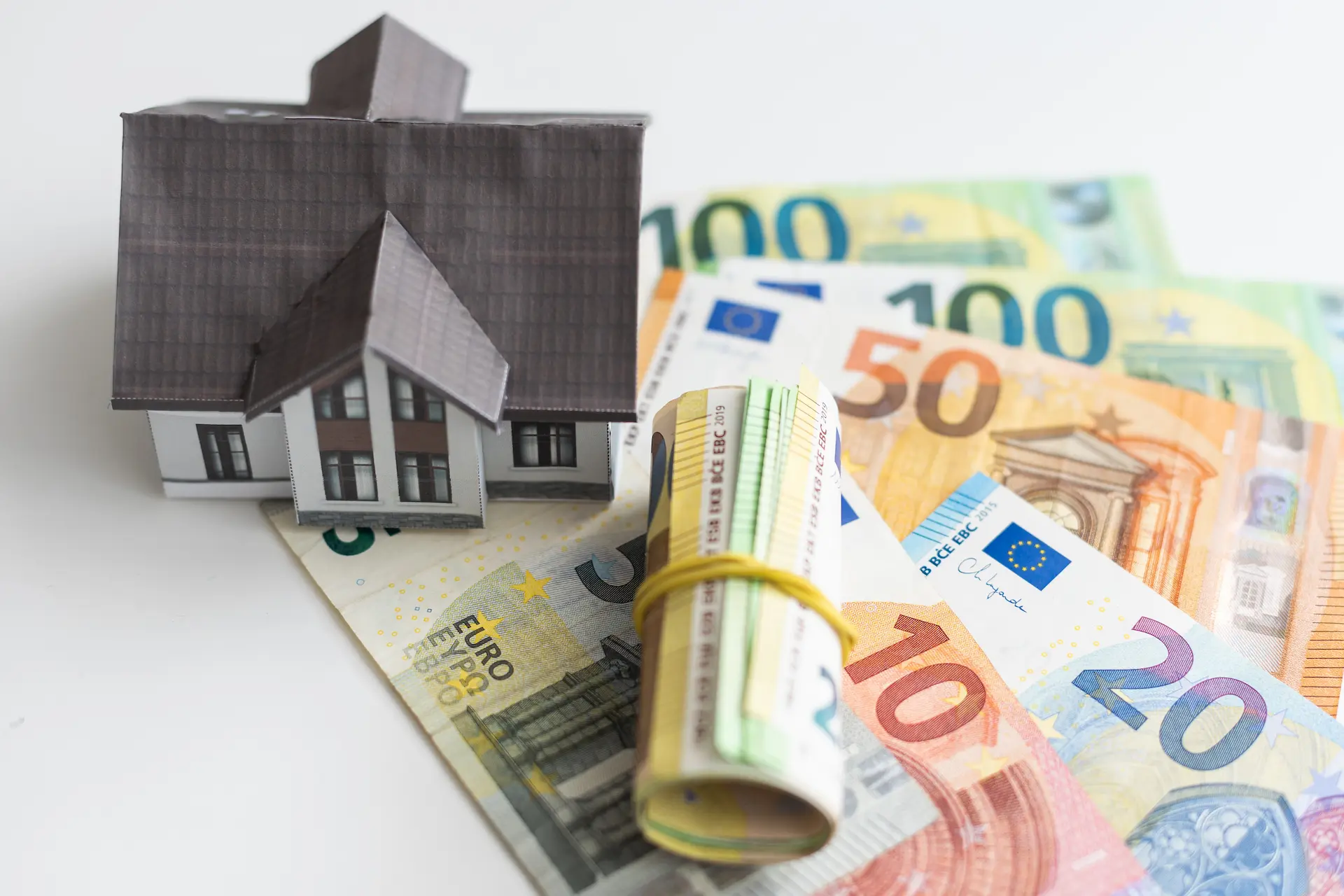 Model house on euro banknotes with a rolled bill in the foreground.