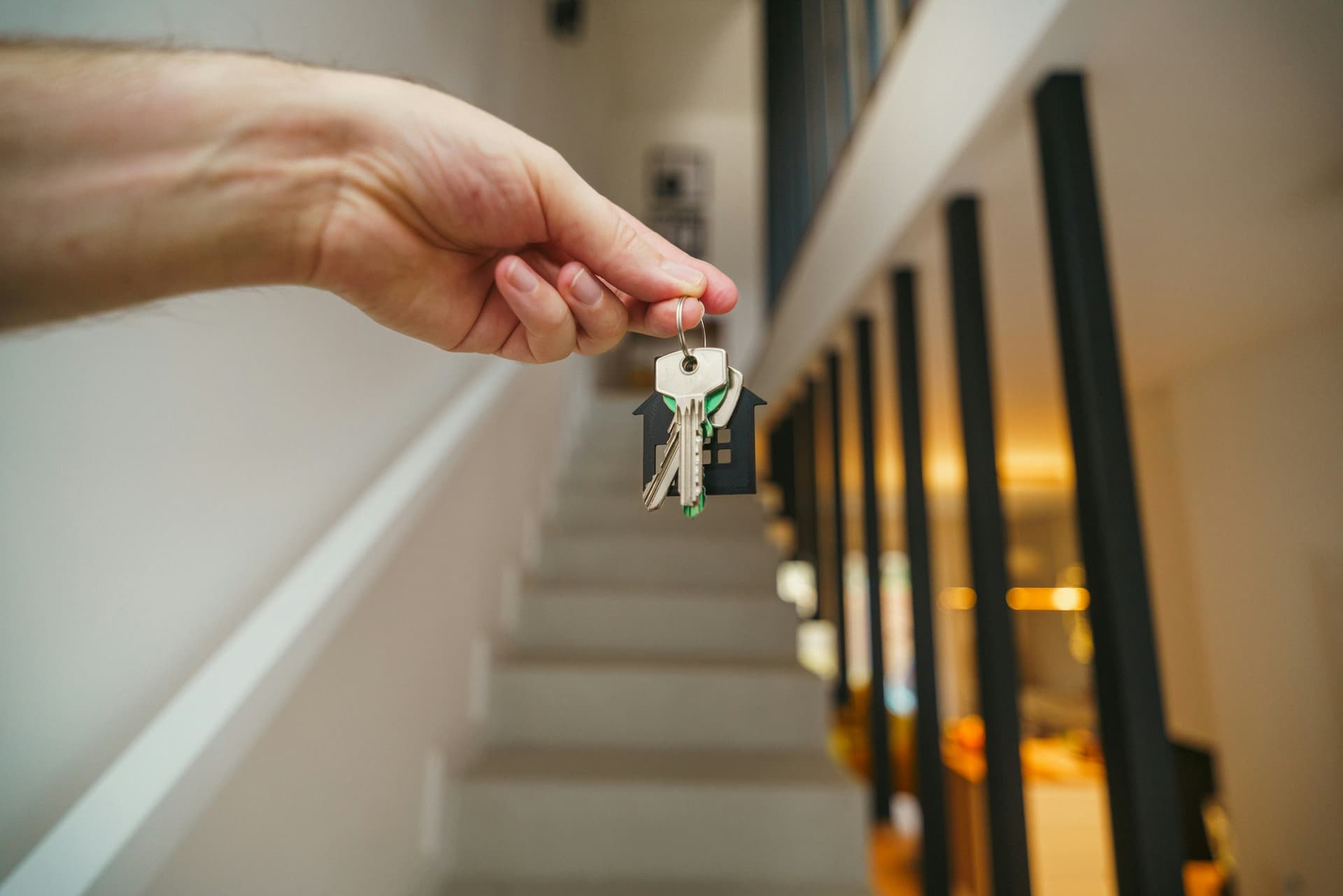 Hand hält Wohnungsschlüssel mit Haus-Anhänger im Treppenhaus – Übergabe einer vermieteten Eigentumswohnung