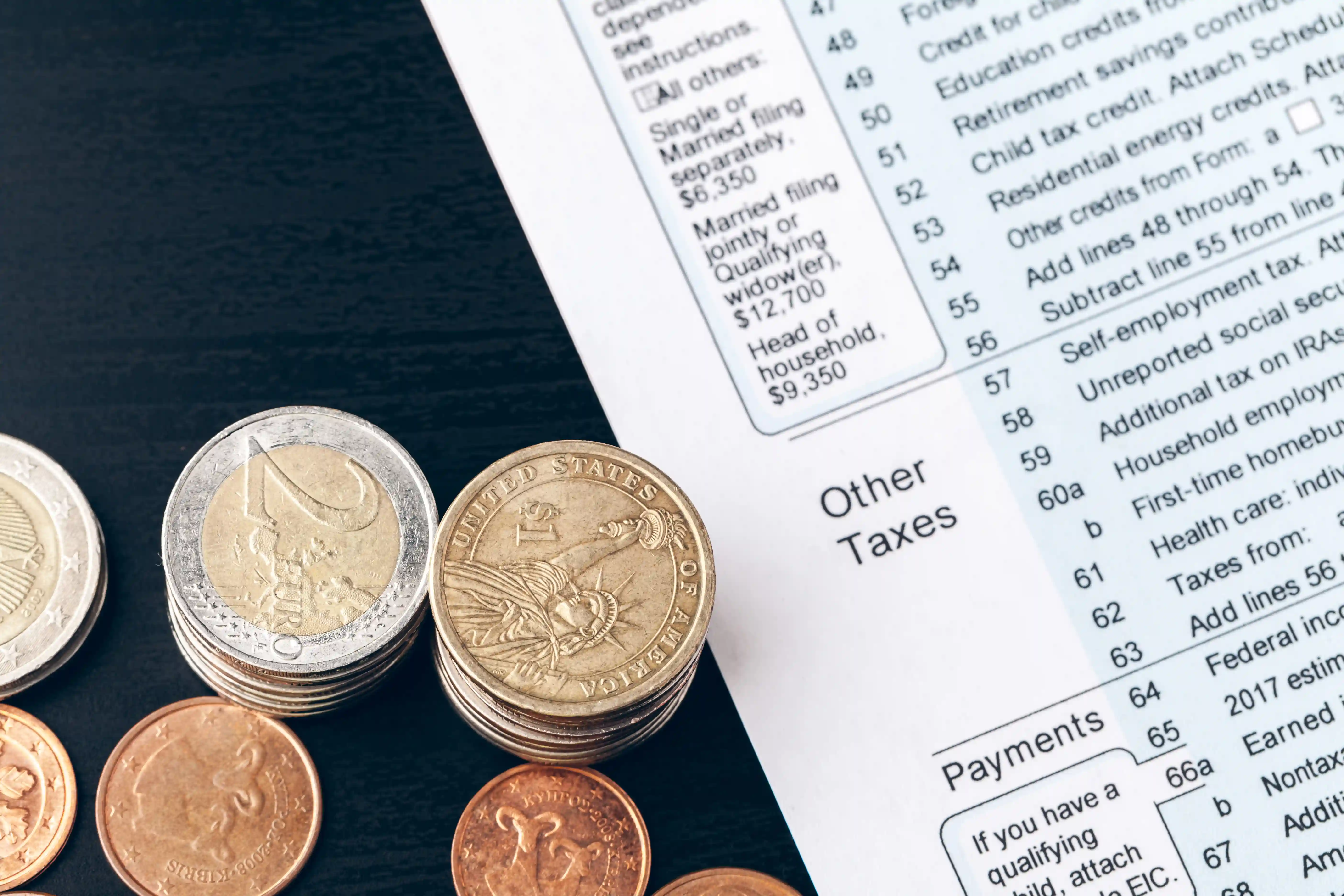 Stacked euro and US dollar coins next to a tax form labeled “Other Taxes.”