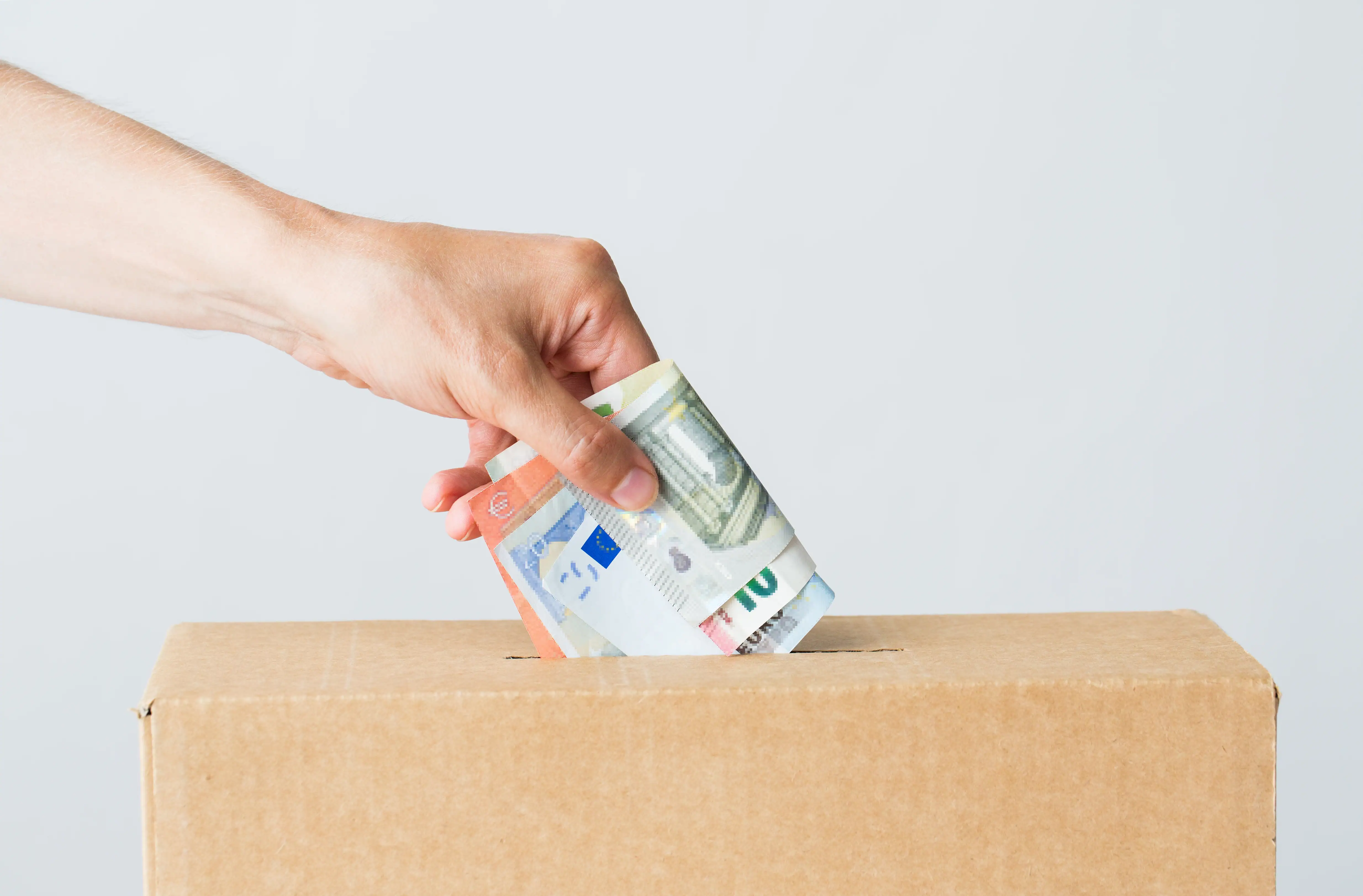 Hand putting euro banknotes into a cardboard donation box.