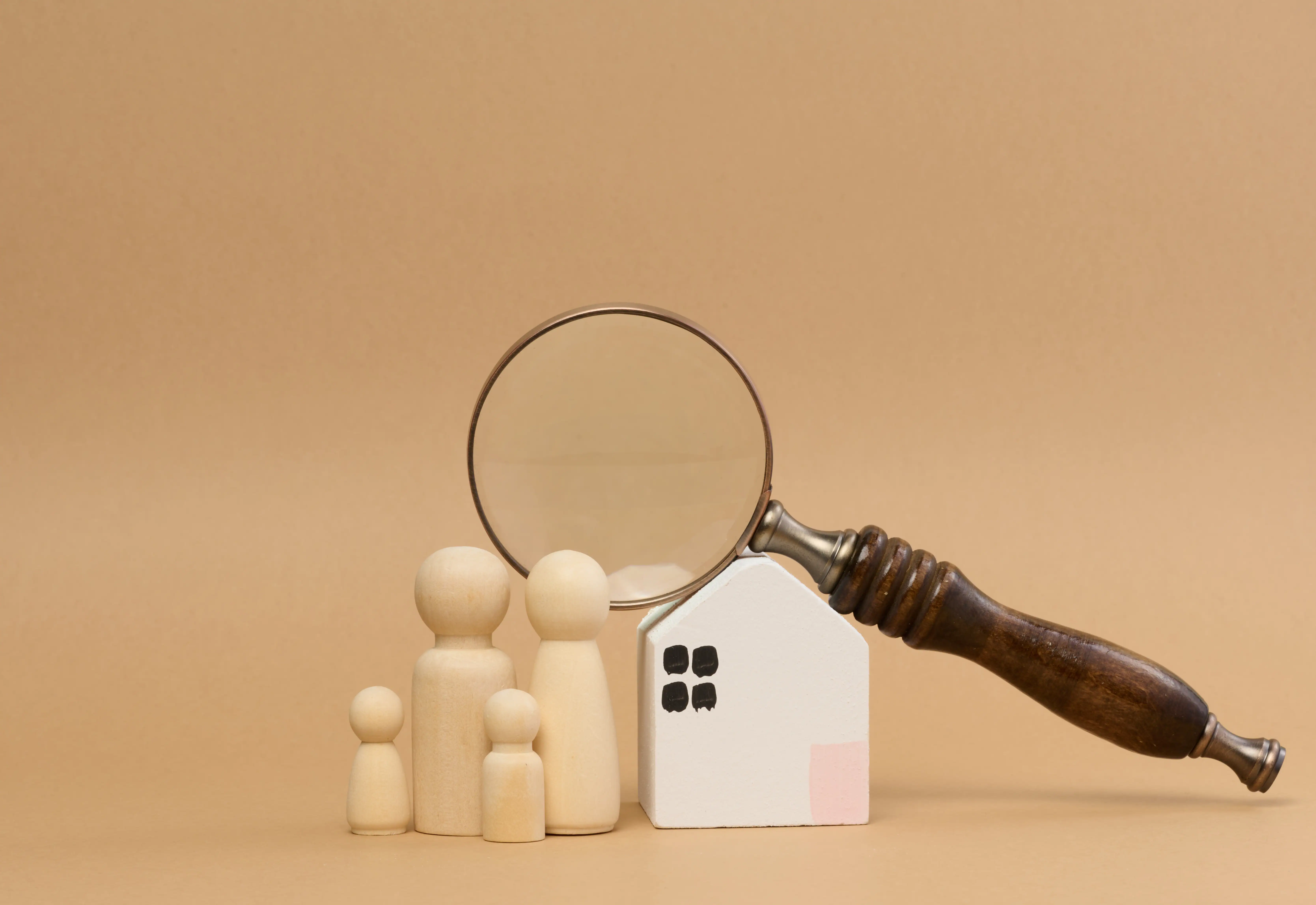 Wooden family figures and a small house with a magnifying glass in front.