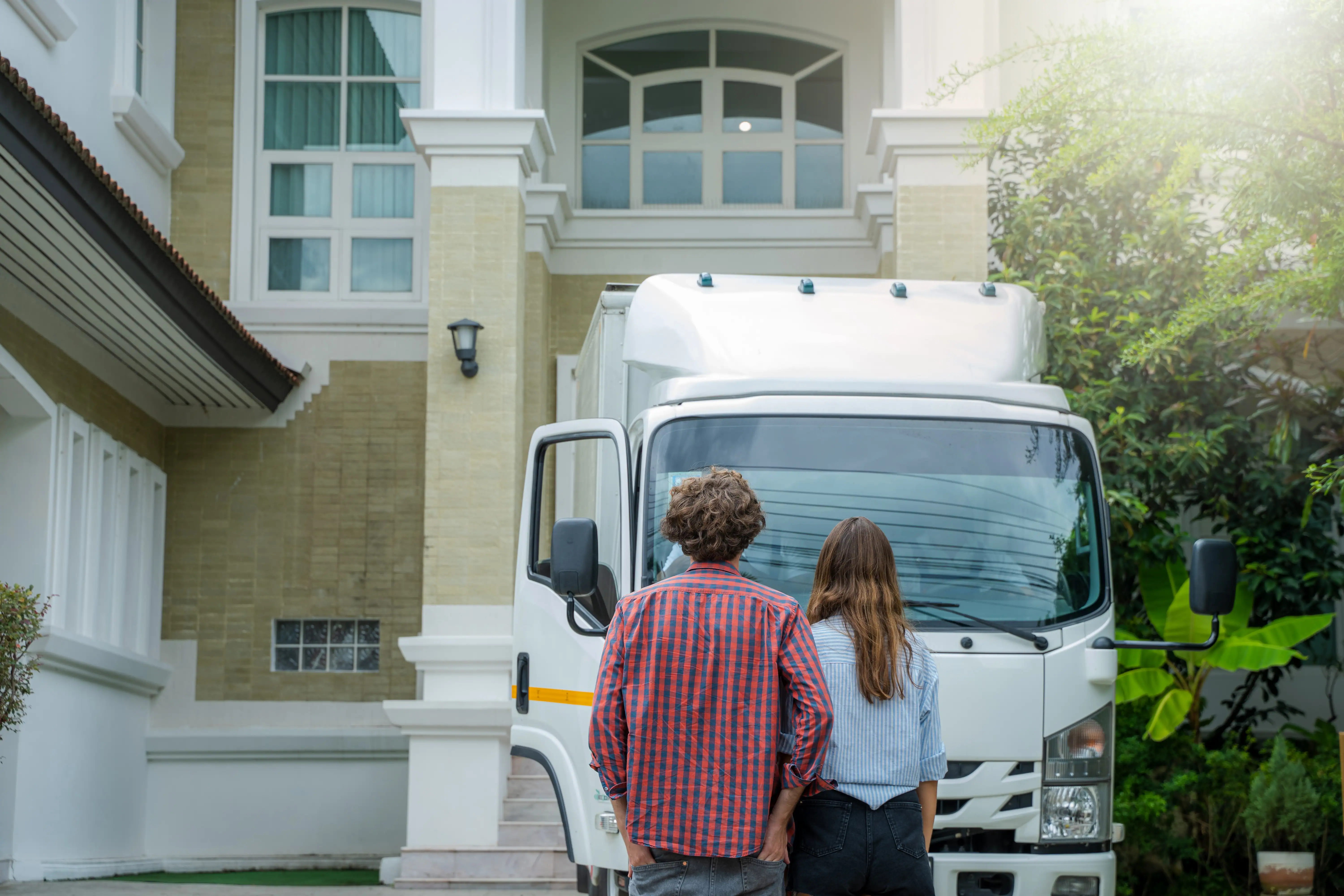 Couple standing in front of a white moving truck at their new home.