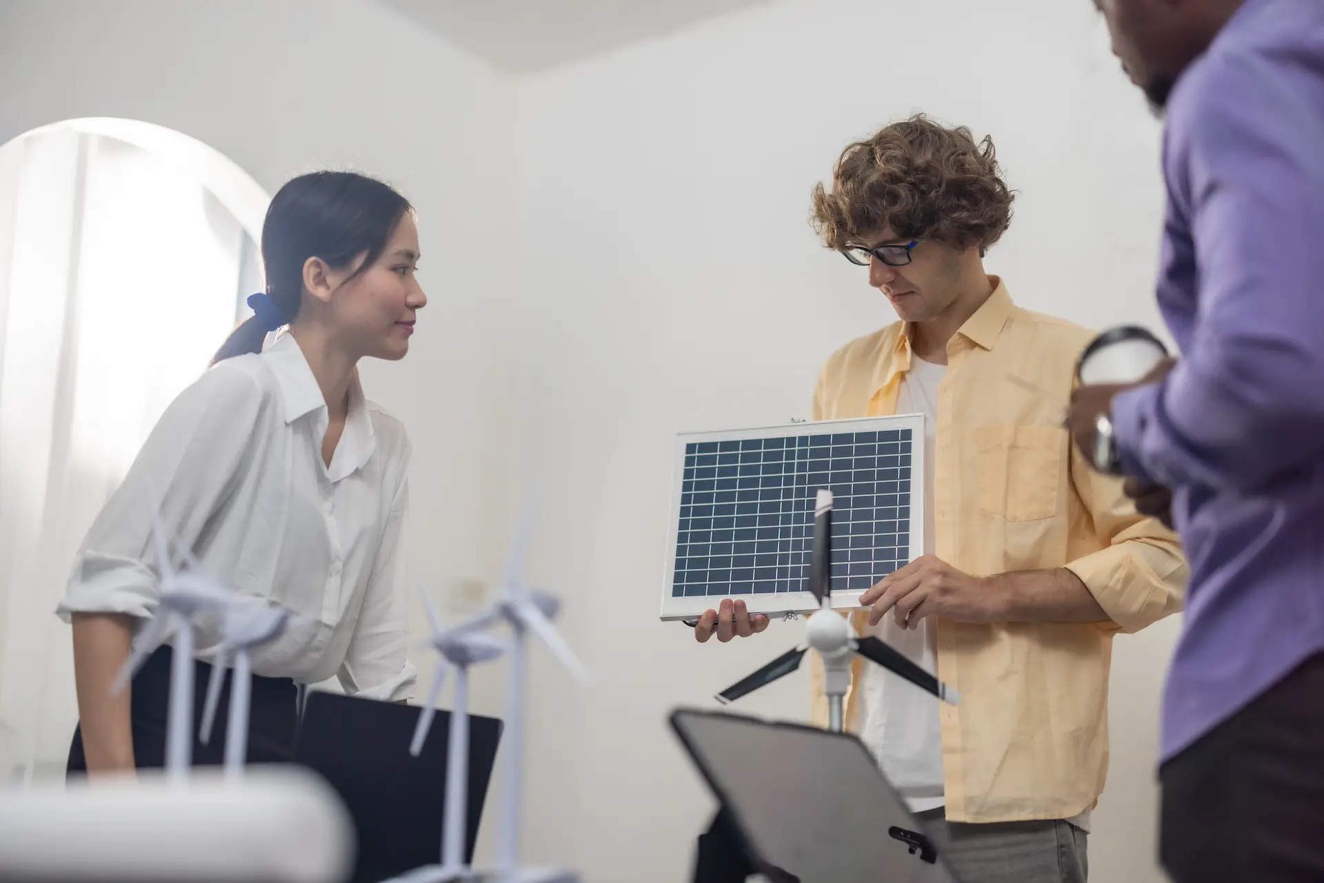 Team discussing balcony PV systems – small solar panel and wind turbine models in an office