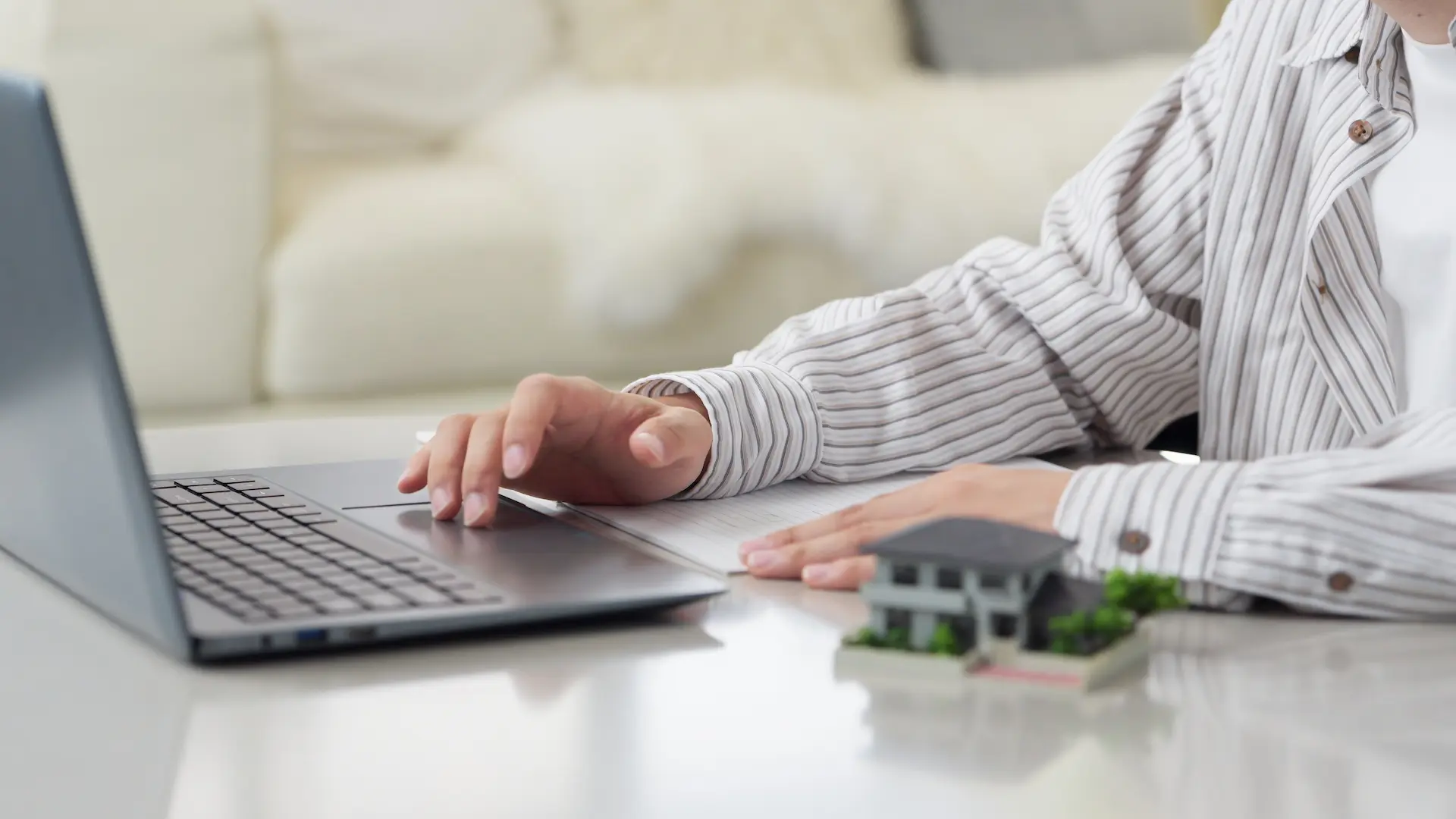 Person researching real estate or rental offers online with miniature house model