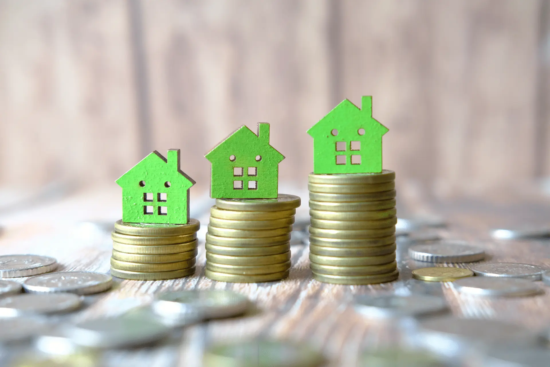 Green house icons placed on stacks of coins illustrating rising housing costs or property values.