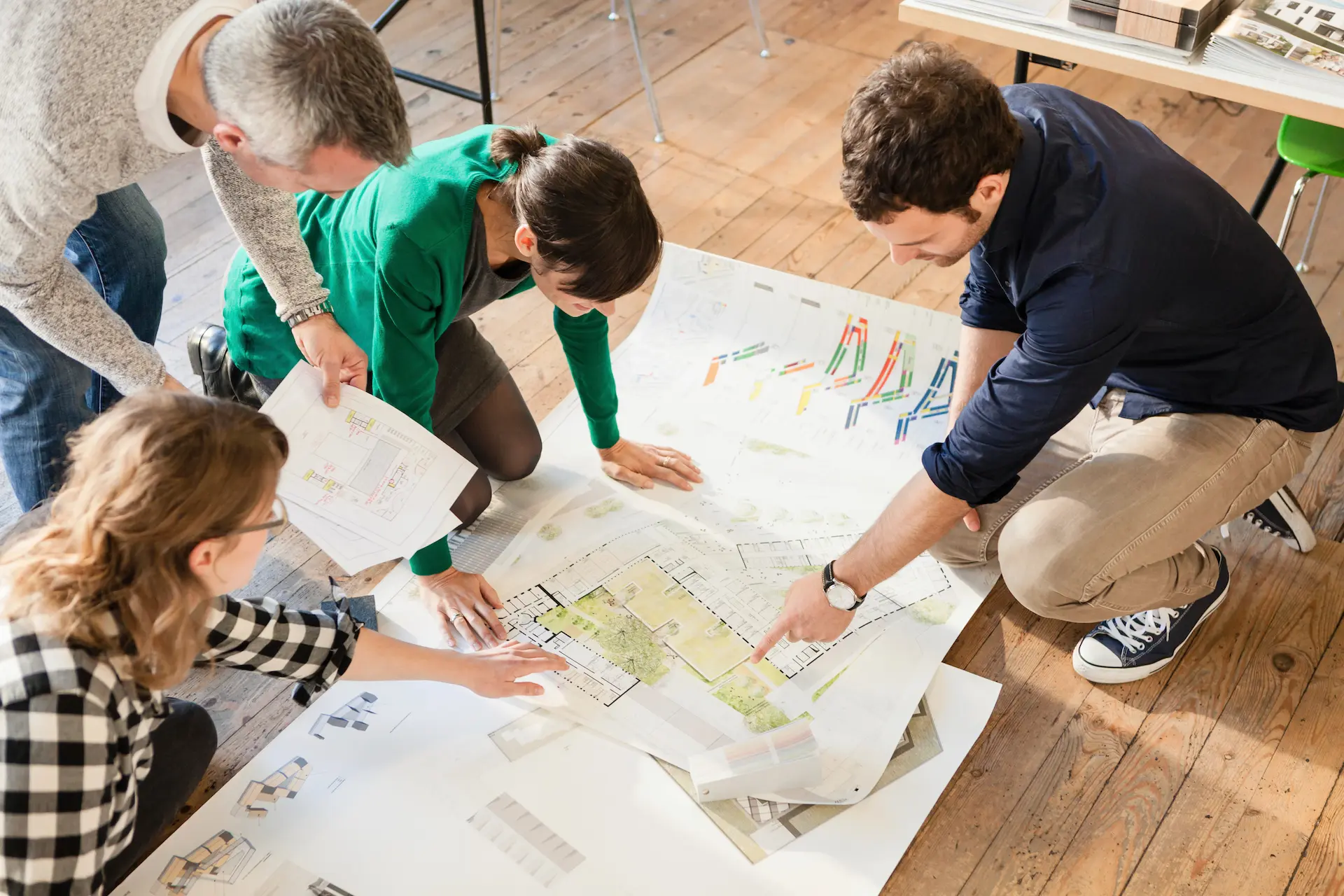 A team of four people kneeling over architectural plans and discussing a project together.