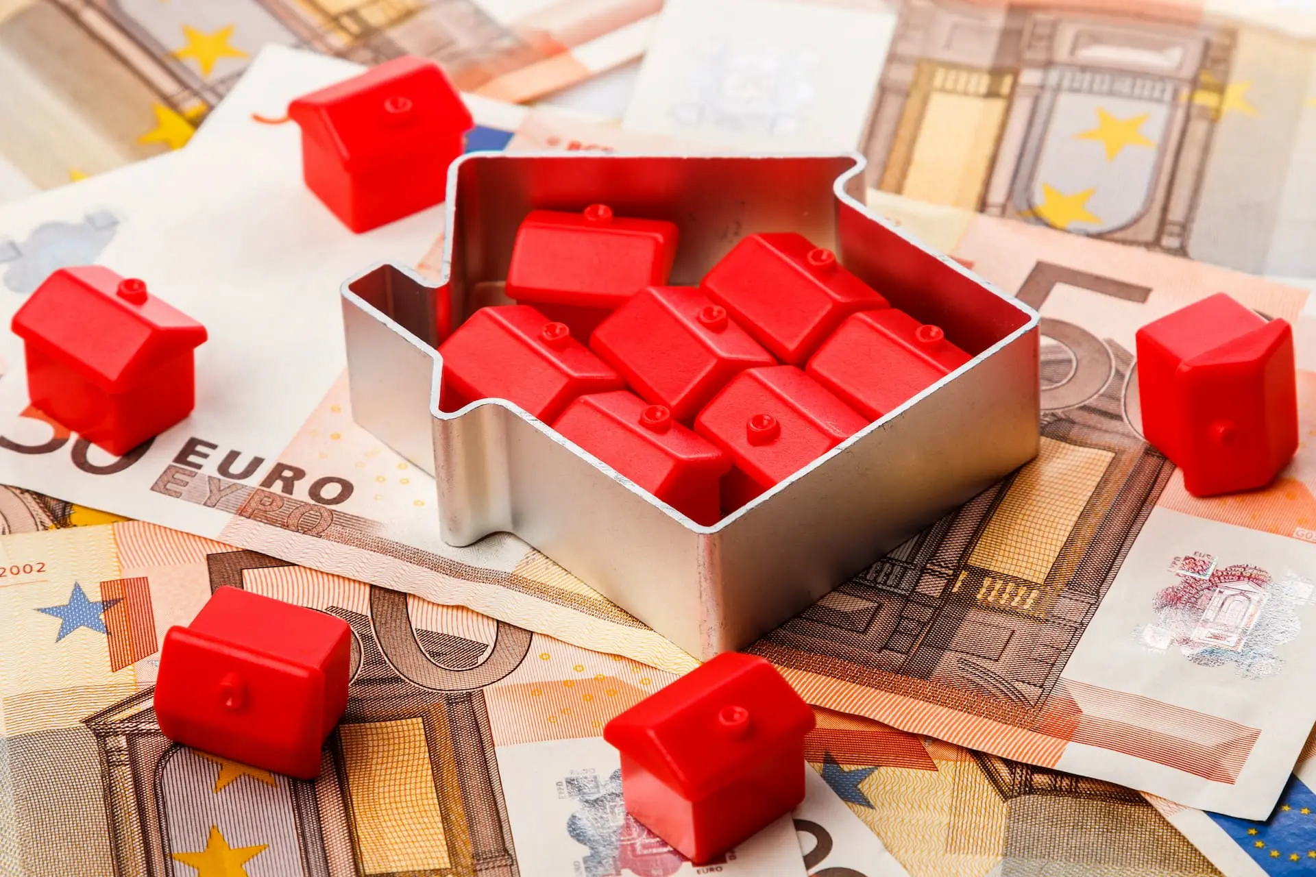 Red house figures on euro banknotes symbolizing real estate prices and purchasing costs in Berlin 2025.