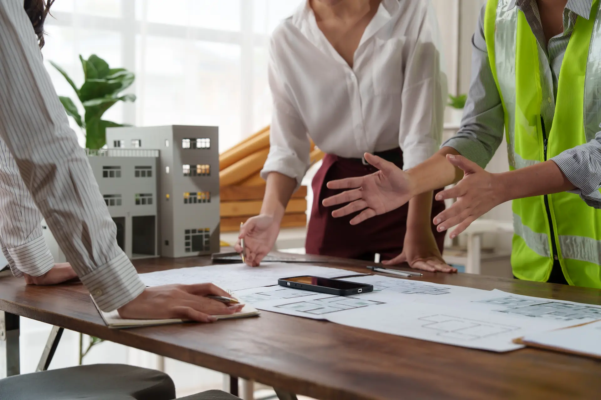 Team of construction planners and architects discussing building plans at a table with architectural models.