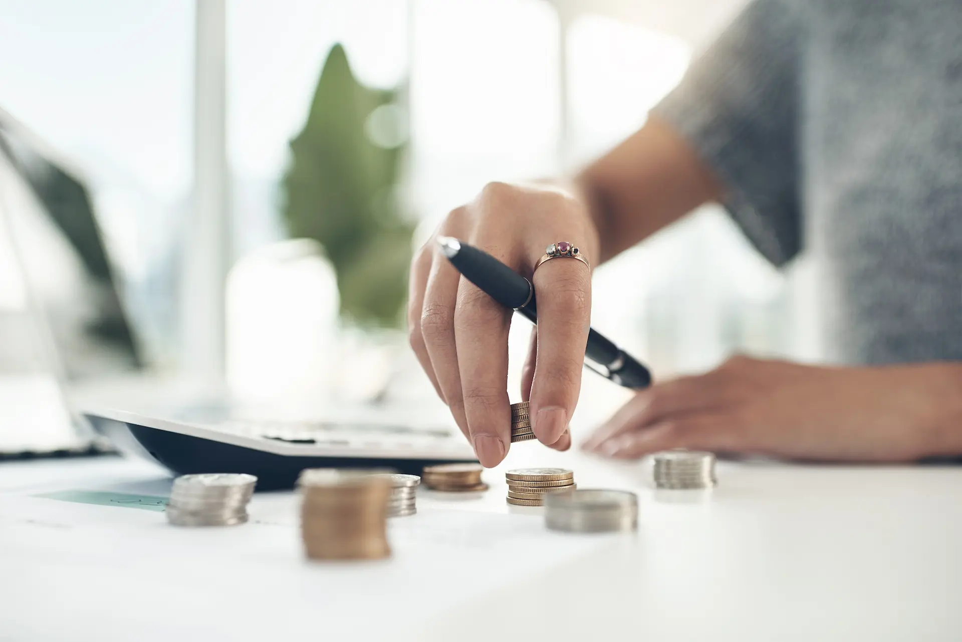 Close-up of a hand stacking coins while planning finances with a pen.