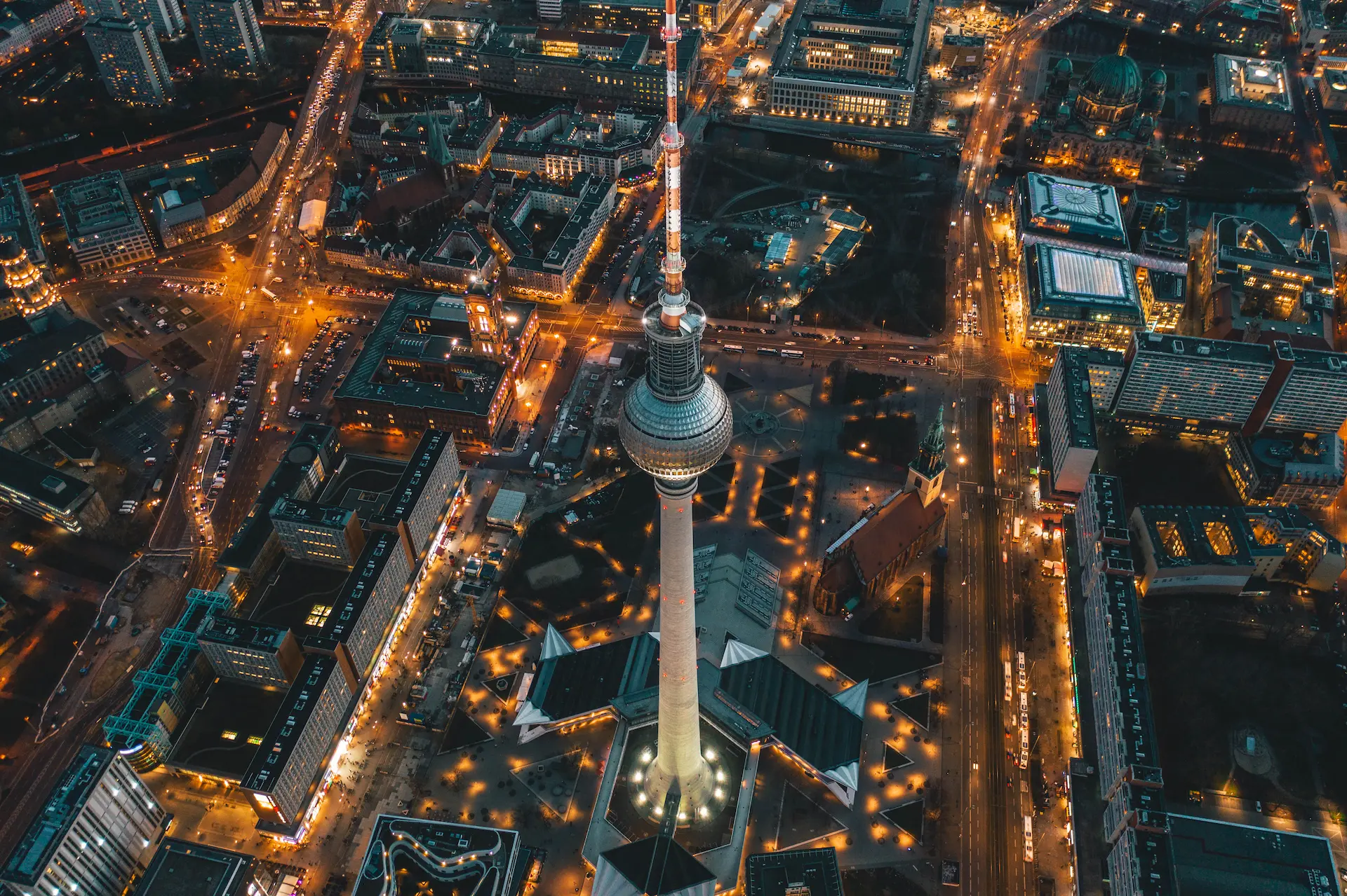 Aerial view of the Berlin TV Tower and Alexanderplatz at night with illuminated streets.