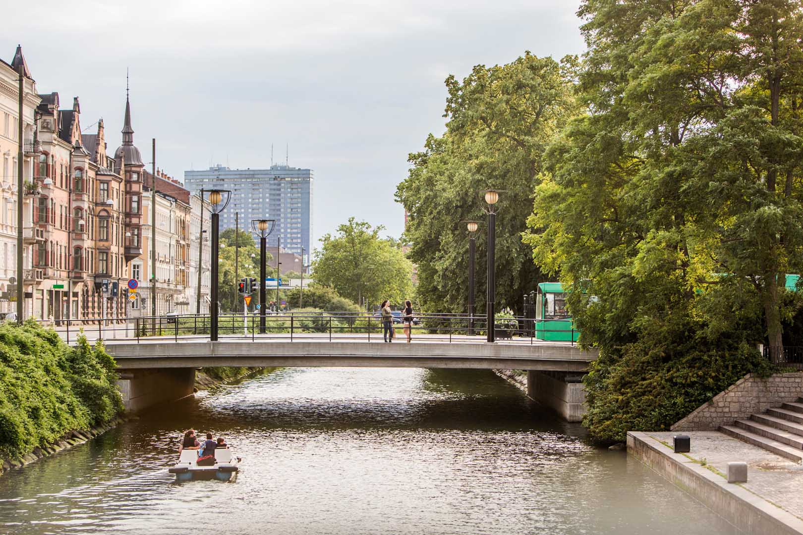 Historic building facades and bridge over a canal in Berlin with people and pedal boat.