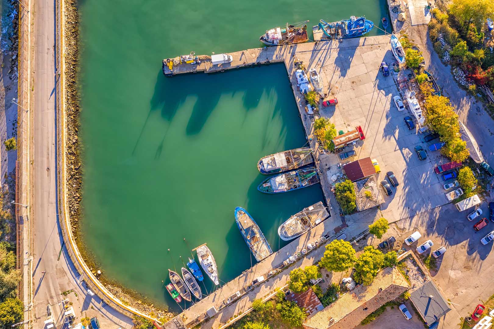 Aerial view of a small harbor with fishing boats and cars on the quay.