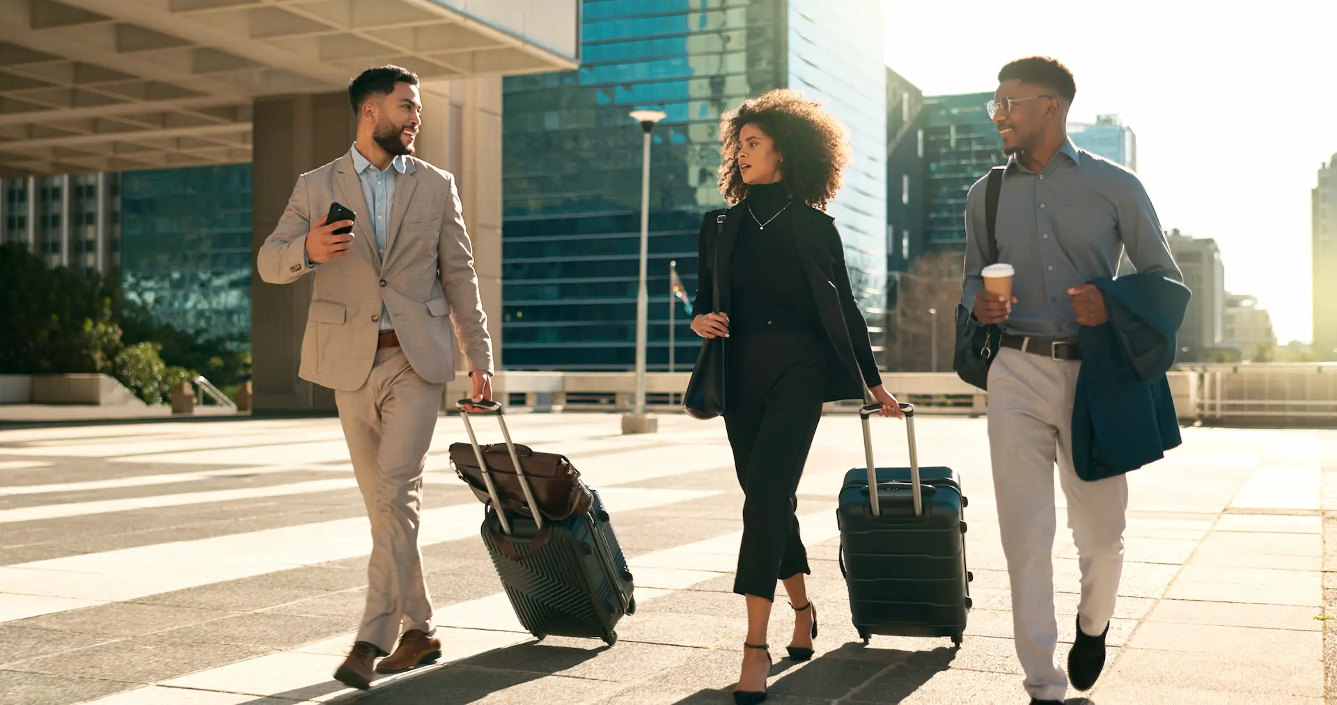 Three business travelers walking with rolling suitcases in a modern city area.