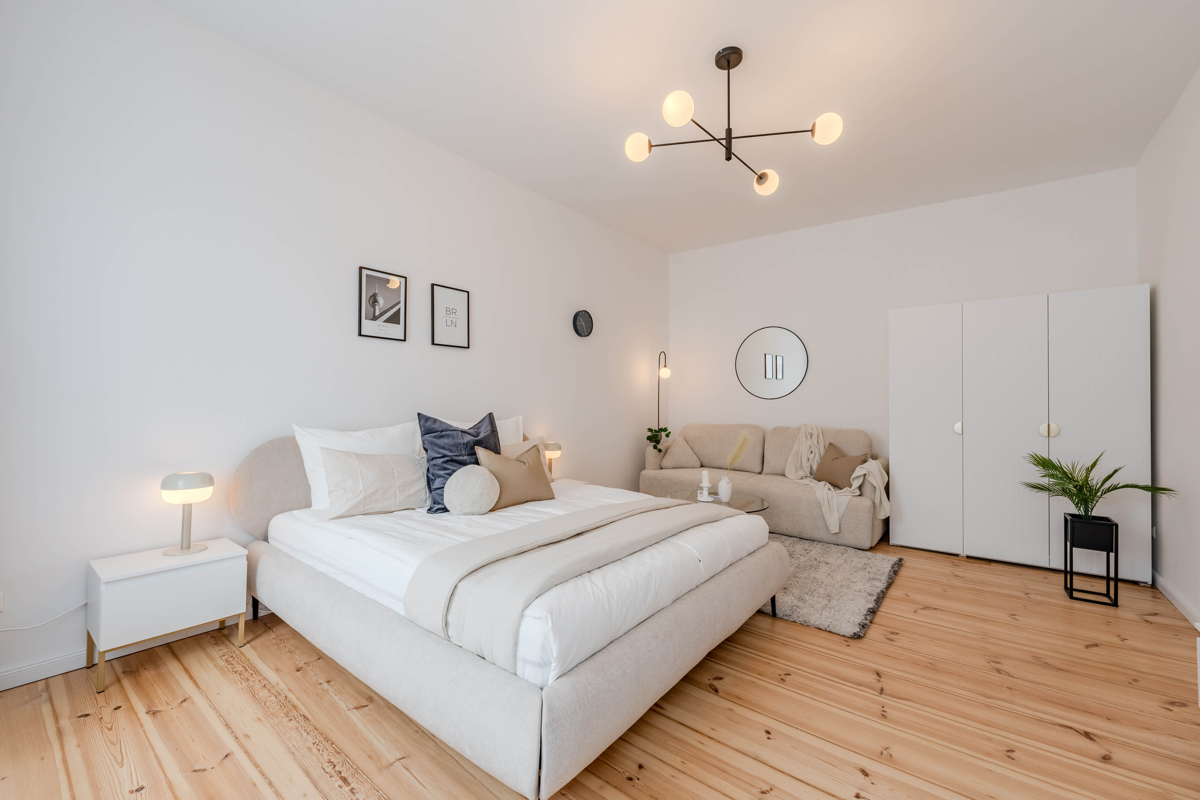 Open-plan living and dining room with a round dining table, white upholstered chairs, grey sofa, large windows, and stylish decorative elements.