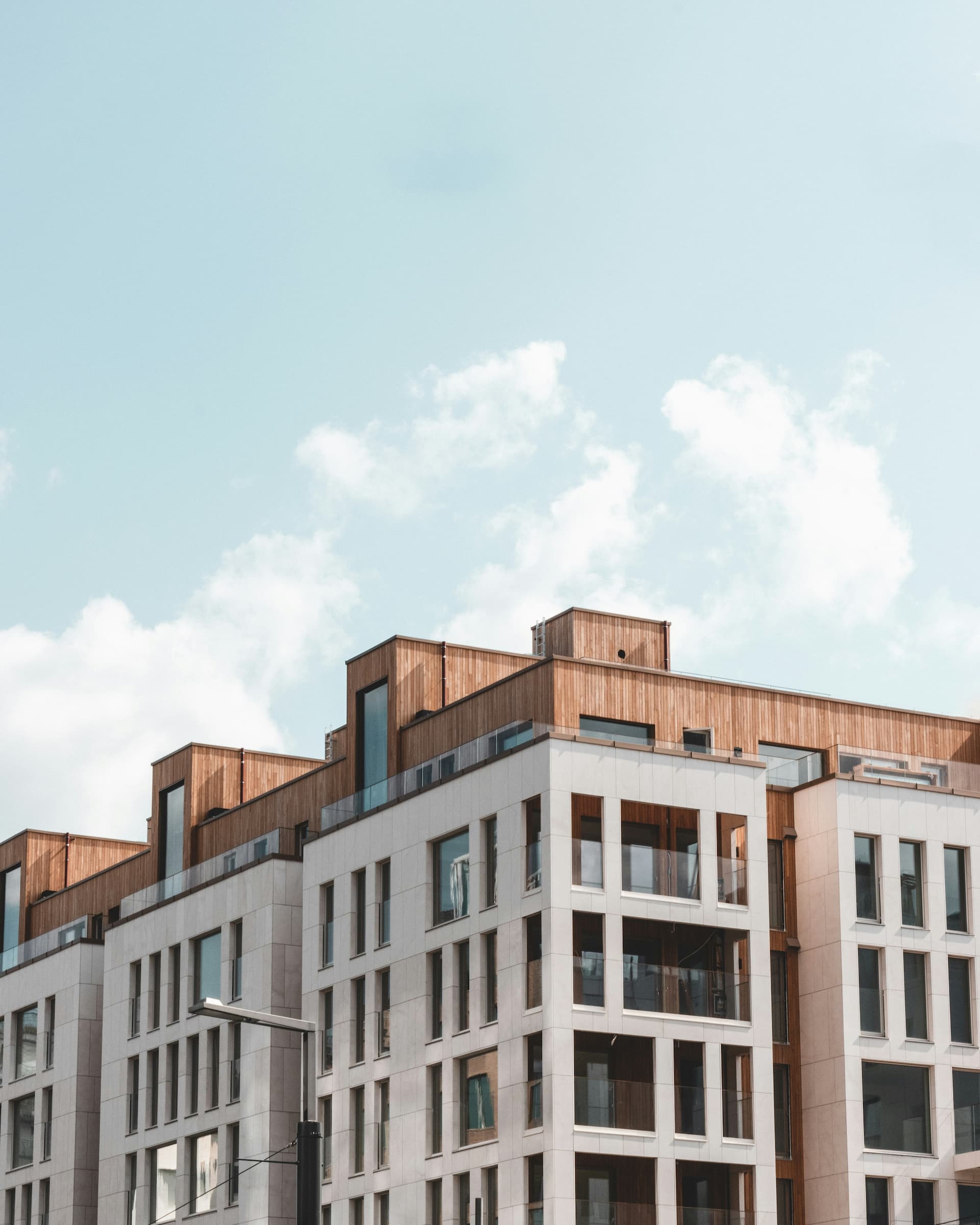 Modernes Mehrfamilienhaus mit Holzverkleidung und Glasbrüstungen vor blauem Himmel – Neubau Immobilien