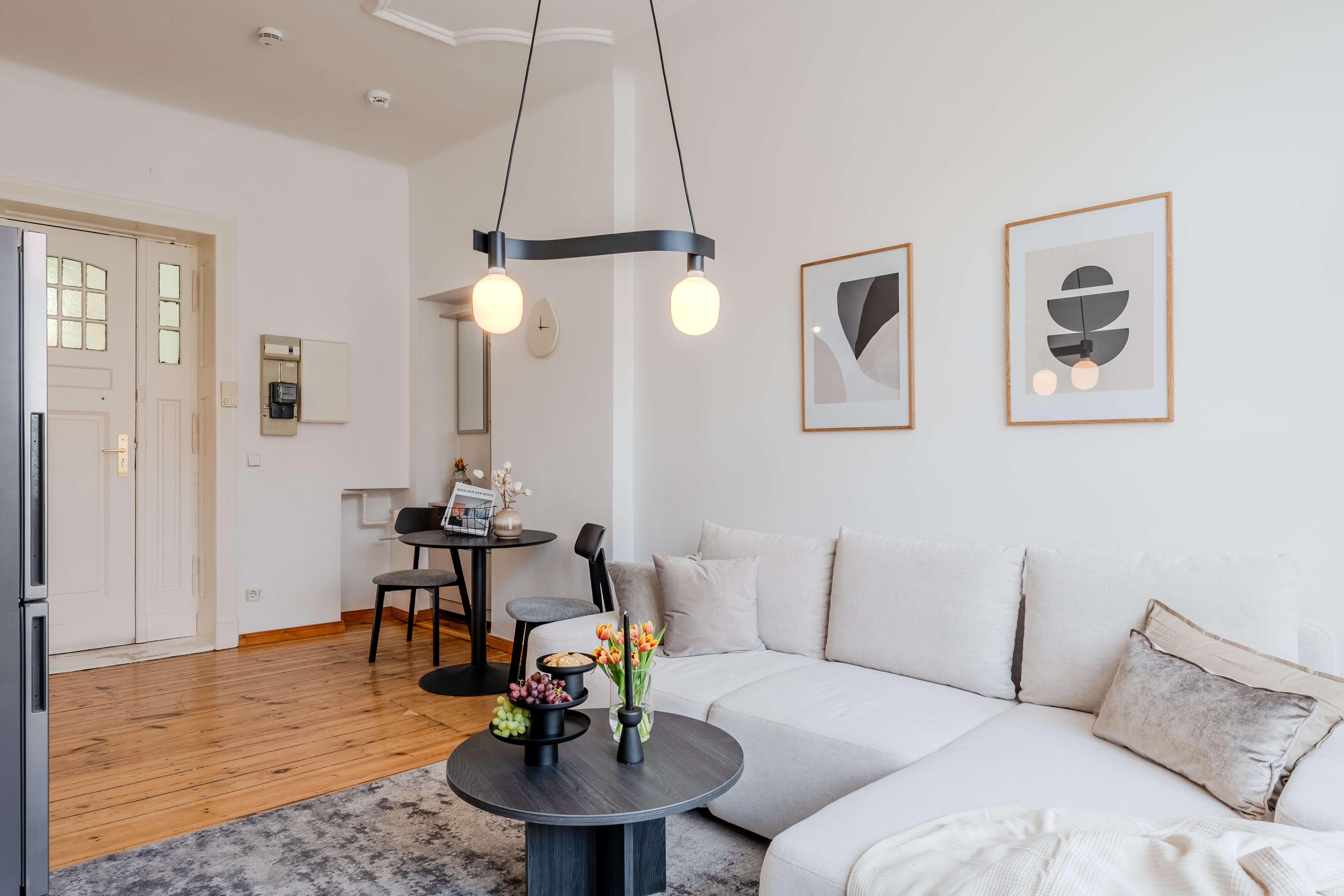Modernly furnished living room with a grey sofa, cozy armchair, round glass coffee table, and an open kitchen in the background.