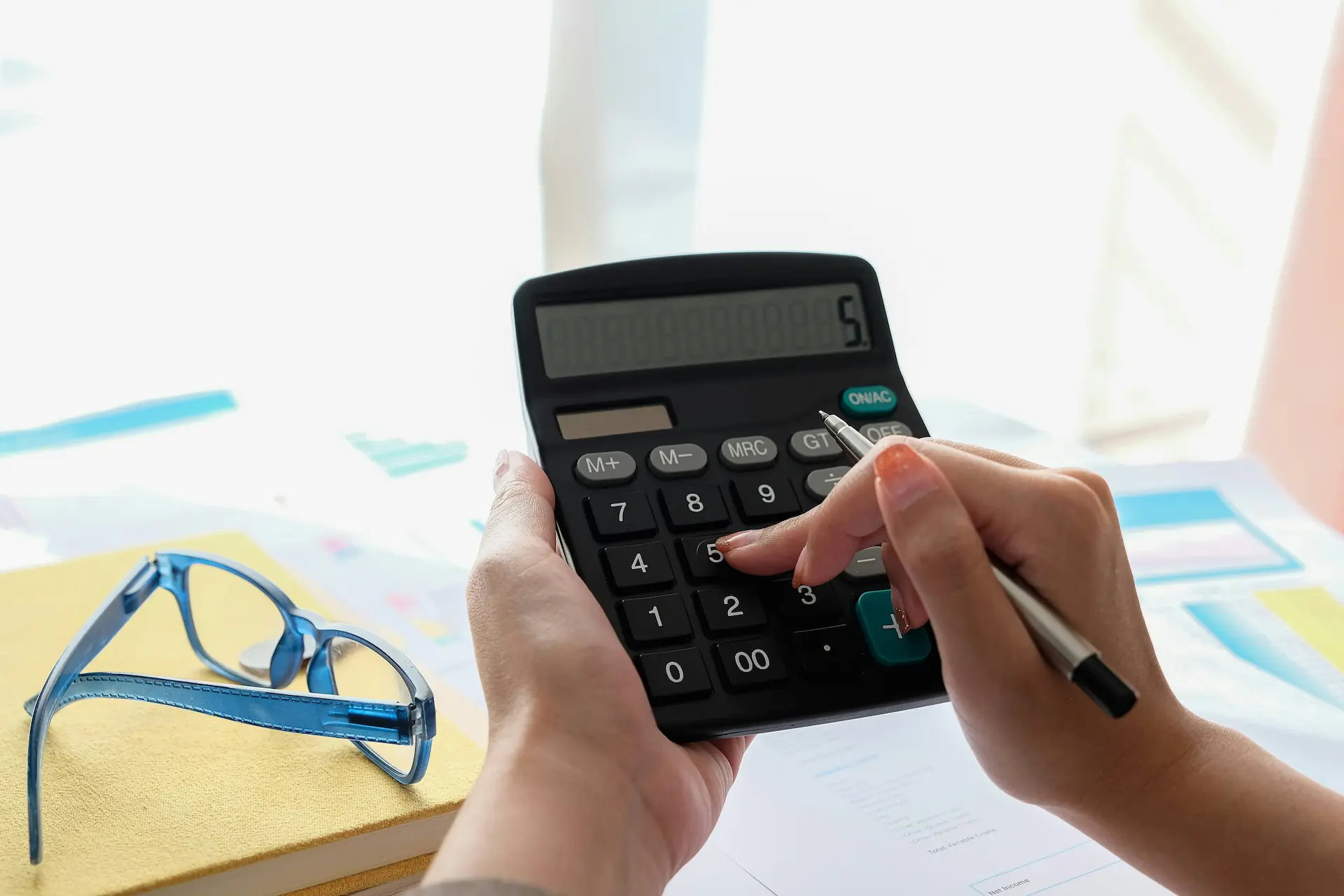 Hands using a calculator next to glasses and documents.