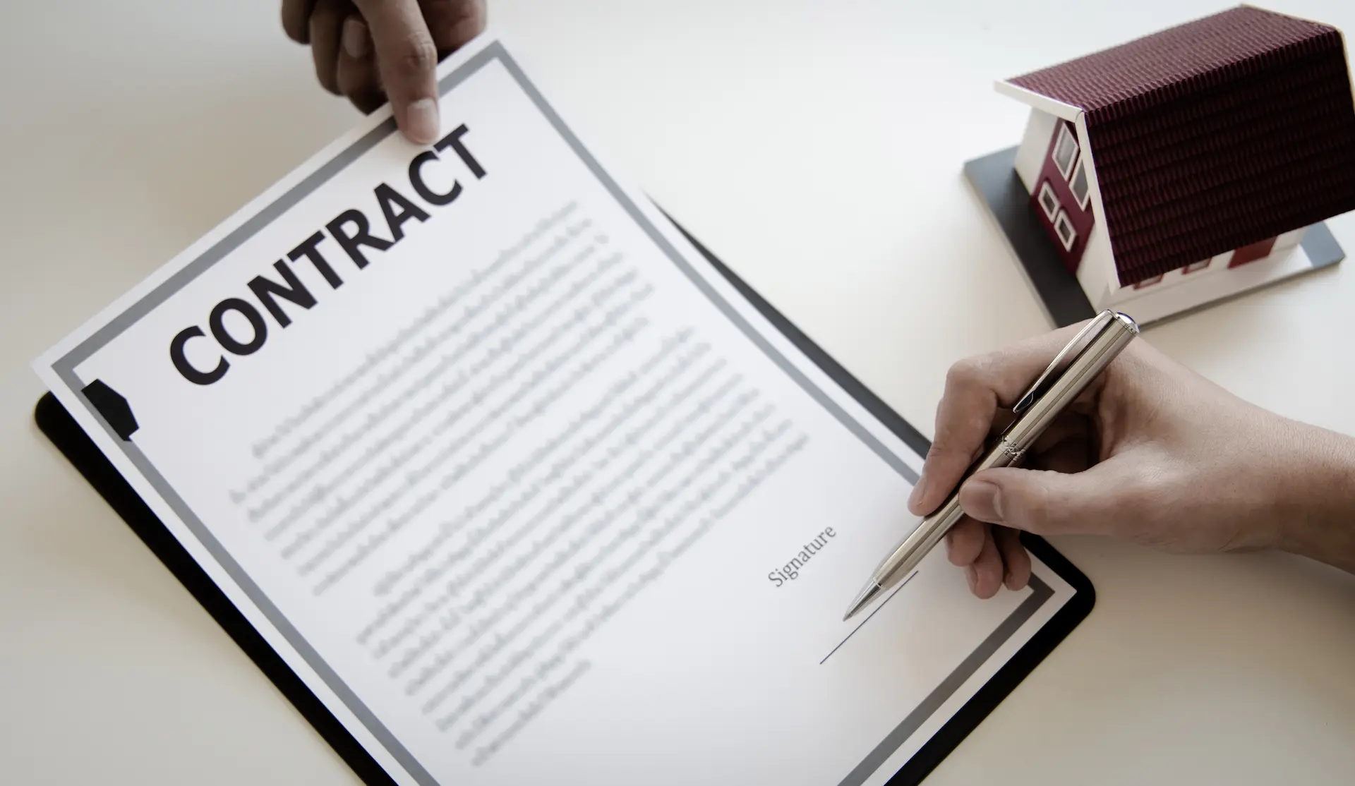 Person signing a contract with a small house model beside it.