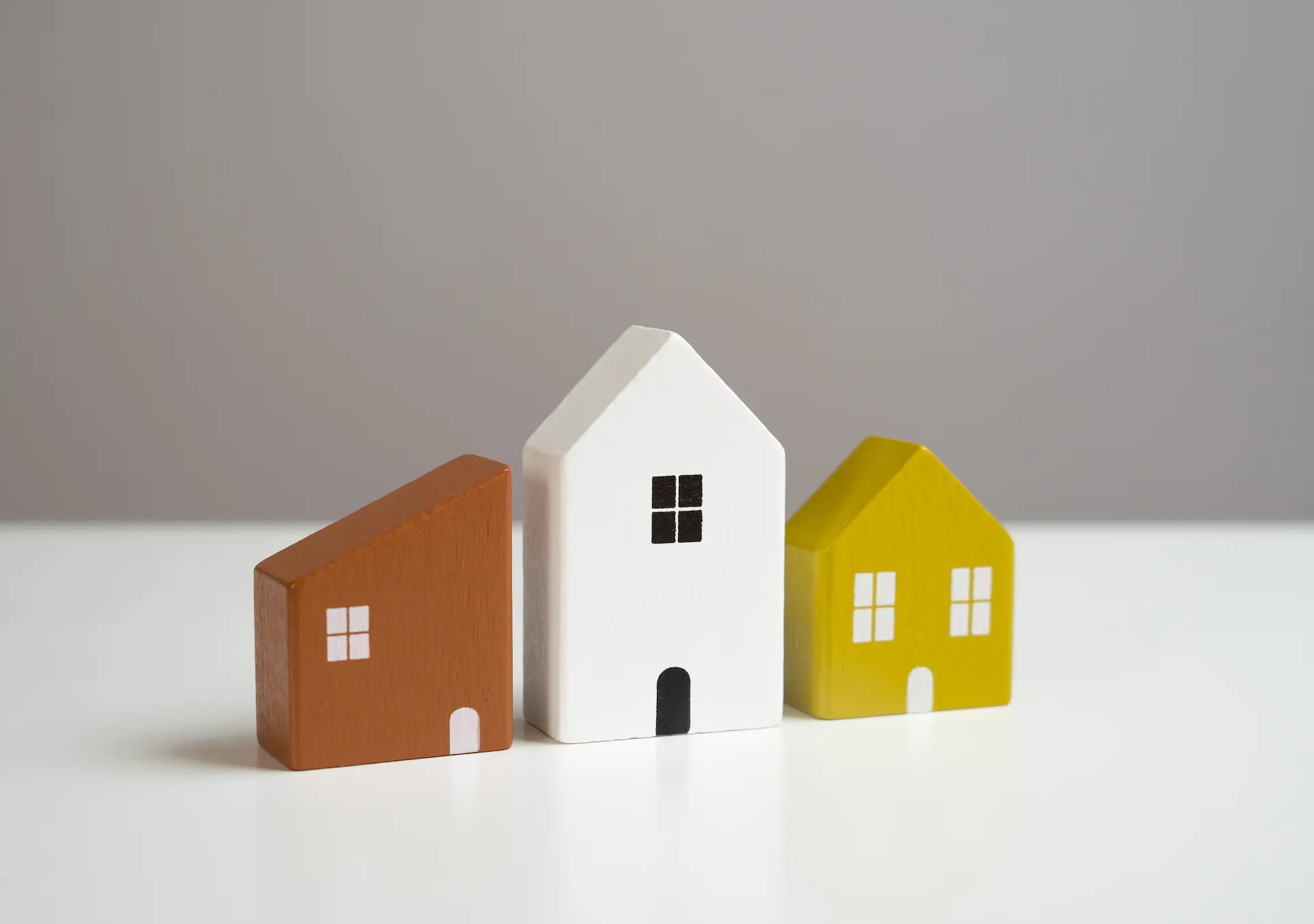 Three colorful wooden house models standing side by side on a light background.