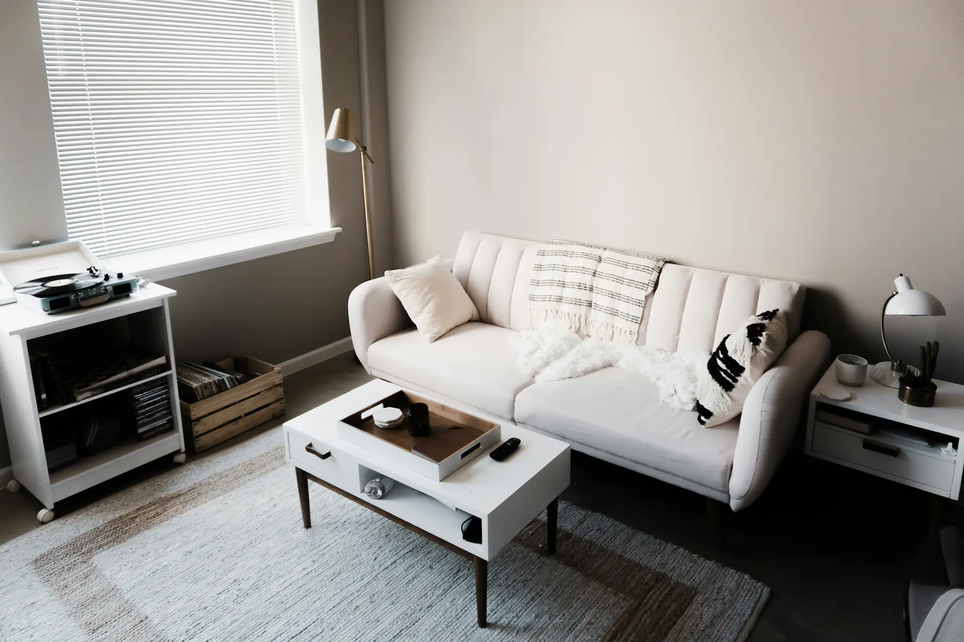 Bright, minimalist living room with a white sofa, coffee table, and record player by the window.