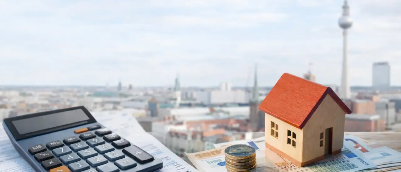Hausmodell, Münzen und Geldscheine neben Taschenrechner vor Stadtpanorama