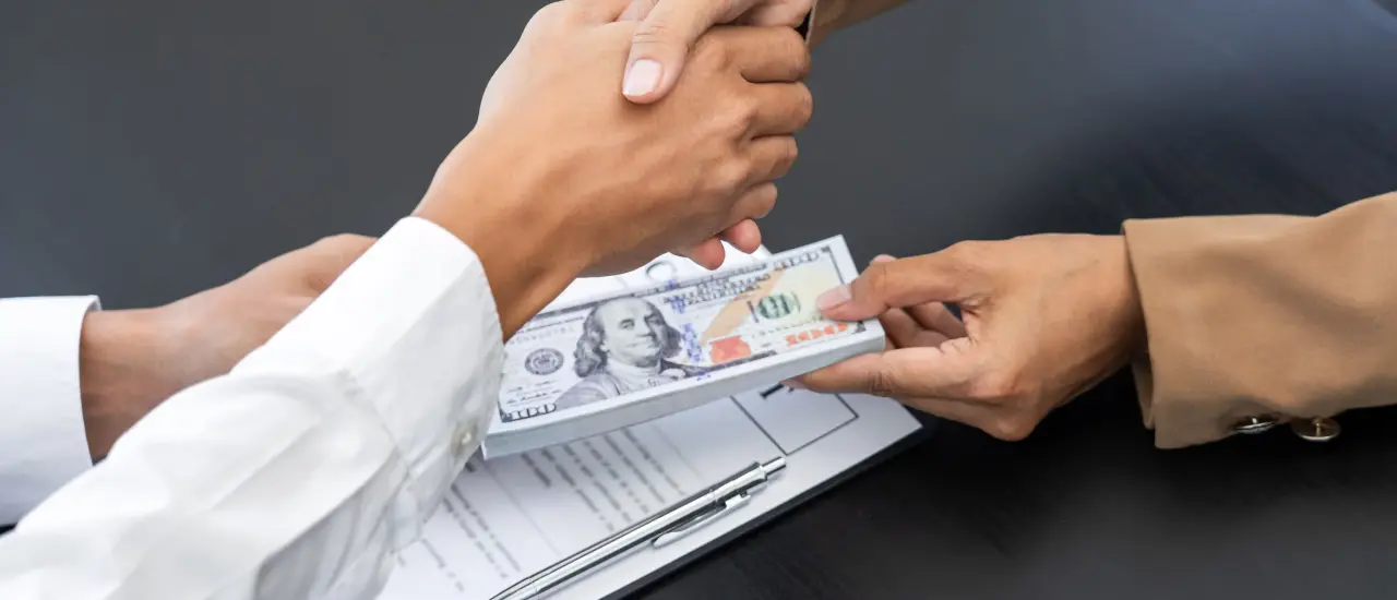 Handschlag mit Bargeld und Vertrag auf dem Tisch