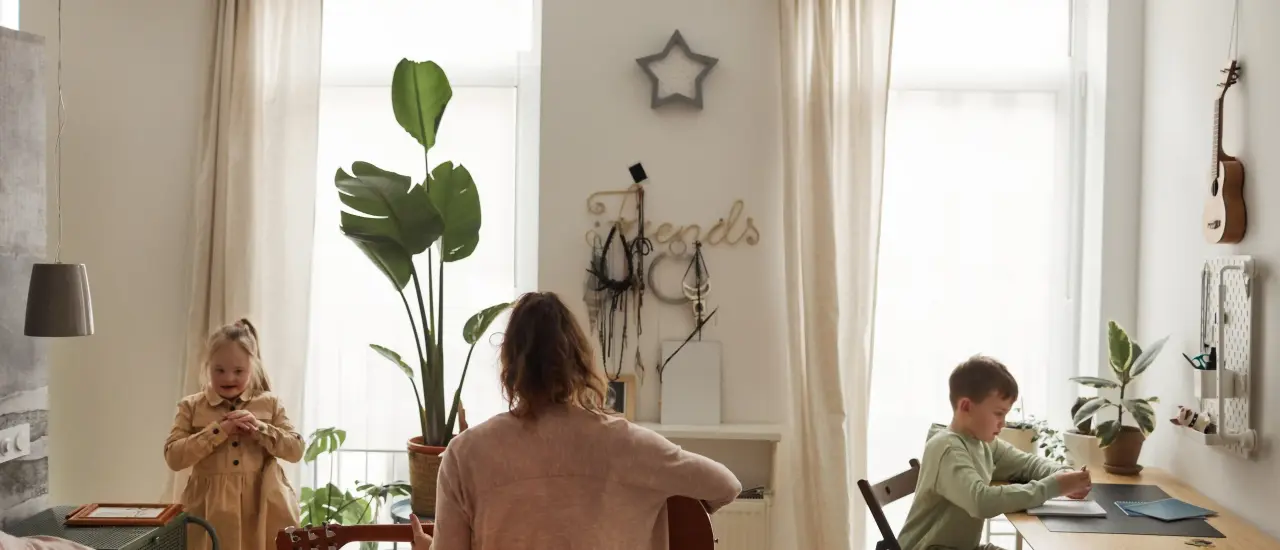 Mutter spielt Gitarre, Kinder beschäftigen sich im hellen Zimmer