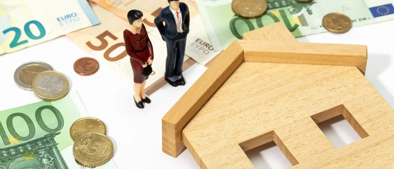 Symbolbild für Immobilienpreise in Berlin mit Geldscheinen, Münzen und Holzhaus.