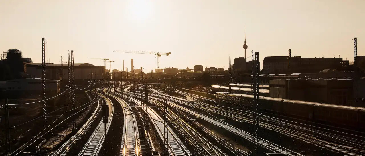 Eisenbahngleise und Skyline von Berlin bei Sonnenuntergang – Symbol für die moderne Infrastruktur der Hauptstadt.