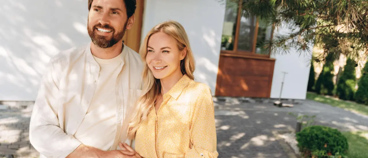 Lächelndes Paar steht vor einem modernen Einfamilienhaus und symbolisiert erfolgreichen Hauskauf.