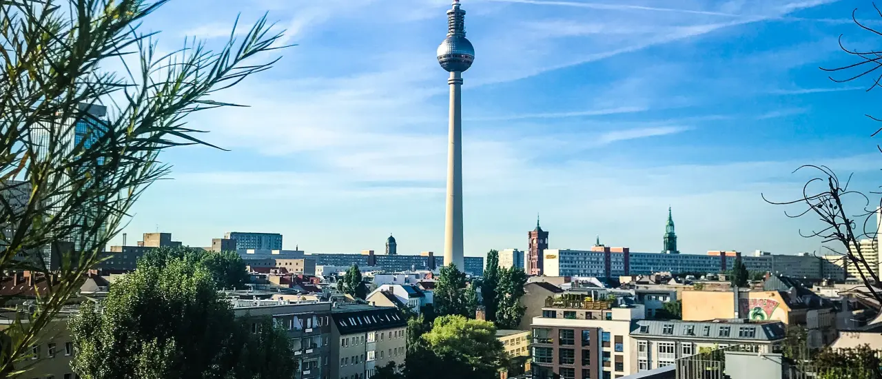 View from a rooftop terrace of the Berlin TV Tower and city skyline under a blue sky