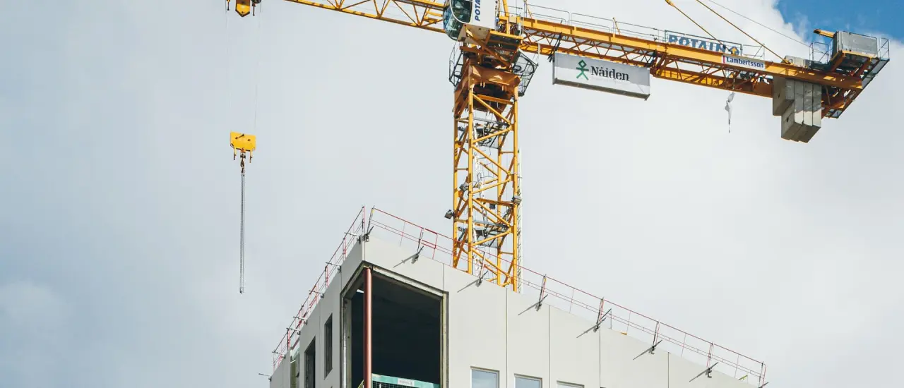 Gelber Baukran über mehrstöckigem Neubau im Rohbau vor blauem Himmel mit Wolken