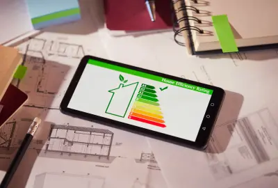 Smartphone mit Energieeffizienz-Bewertung eines Hauses auf Bauplänen und Notizen.