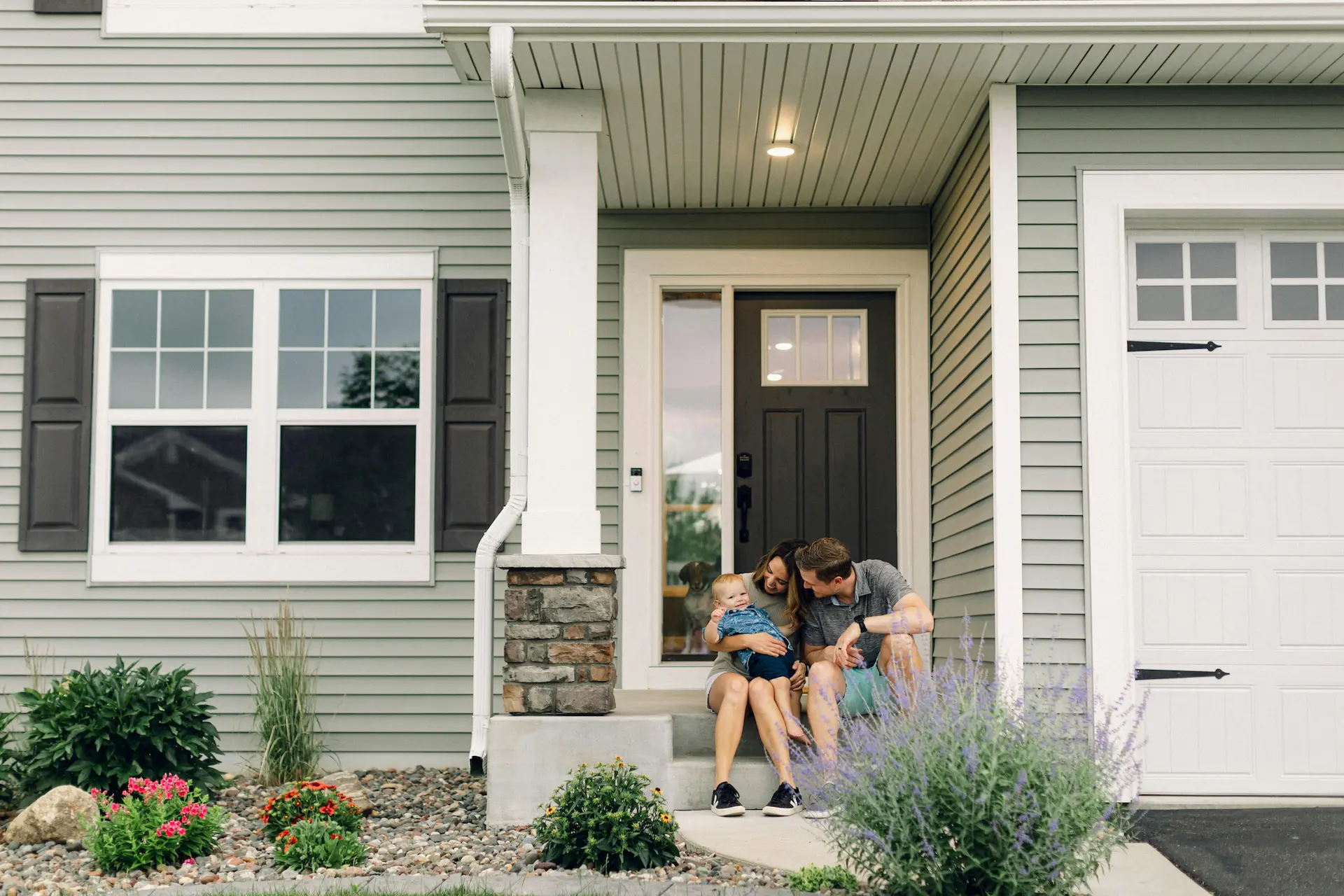 Family with baby sitting on the porch in front of their home.