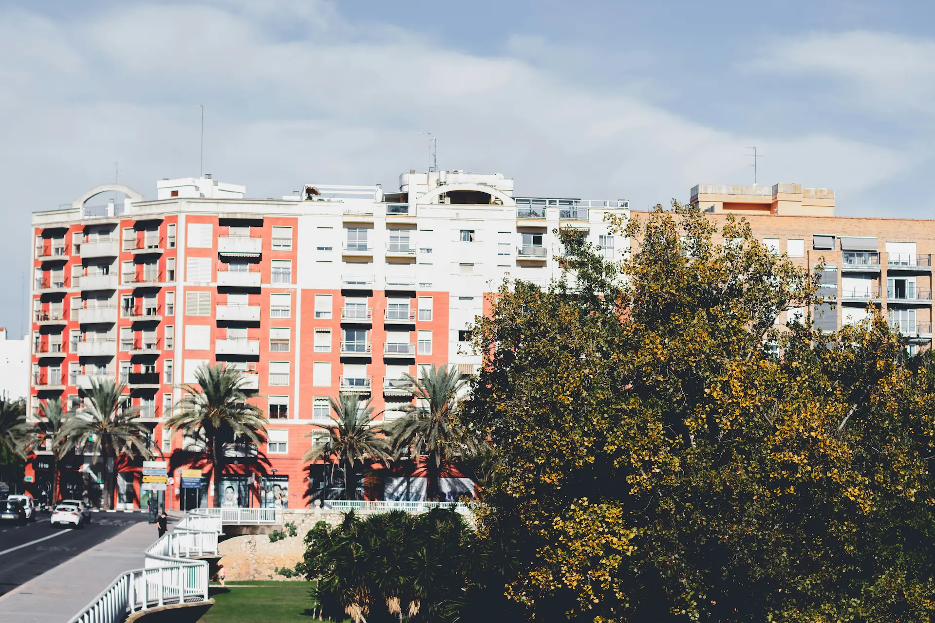 Multi-story apartment building with balconies and palm trees along a city street.