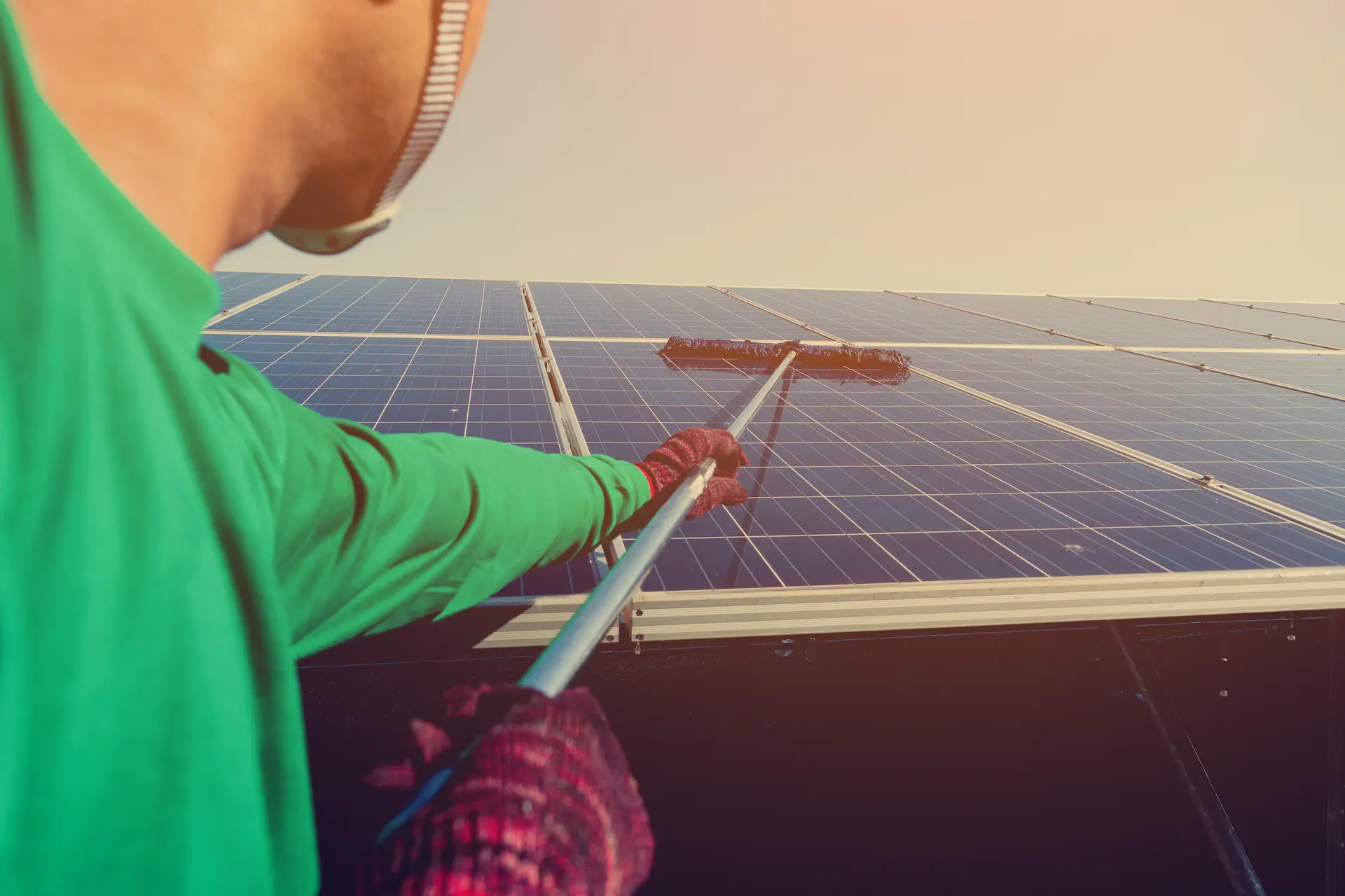 Person cleaning solar panels on a roof with a brush