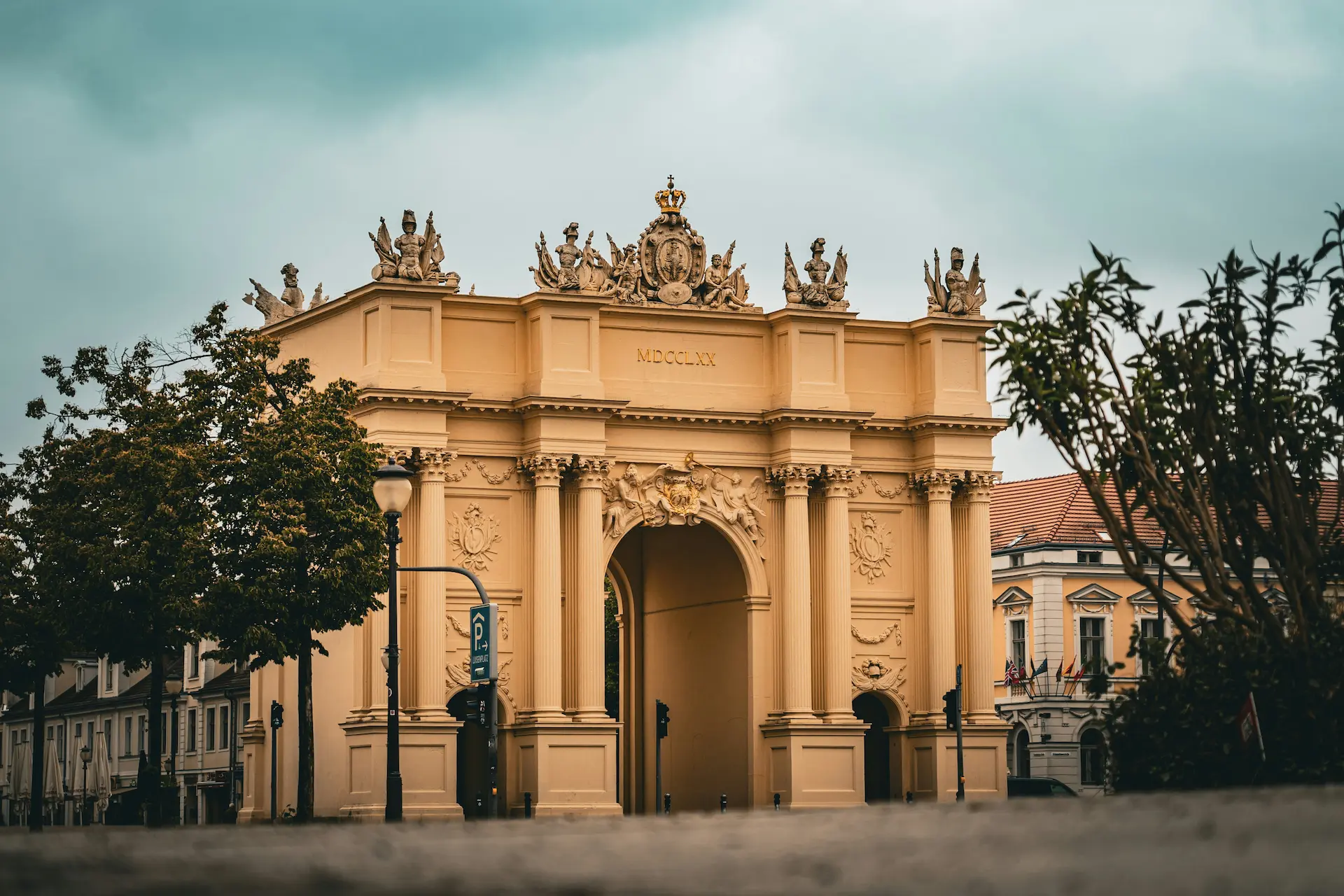 Neoclassical triumphal arch with sculptures and columns on a city street.