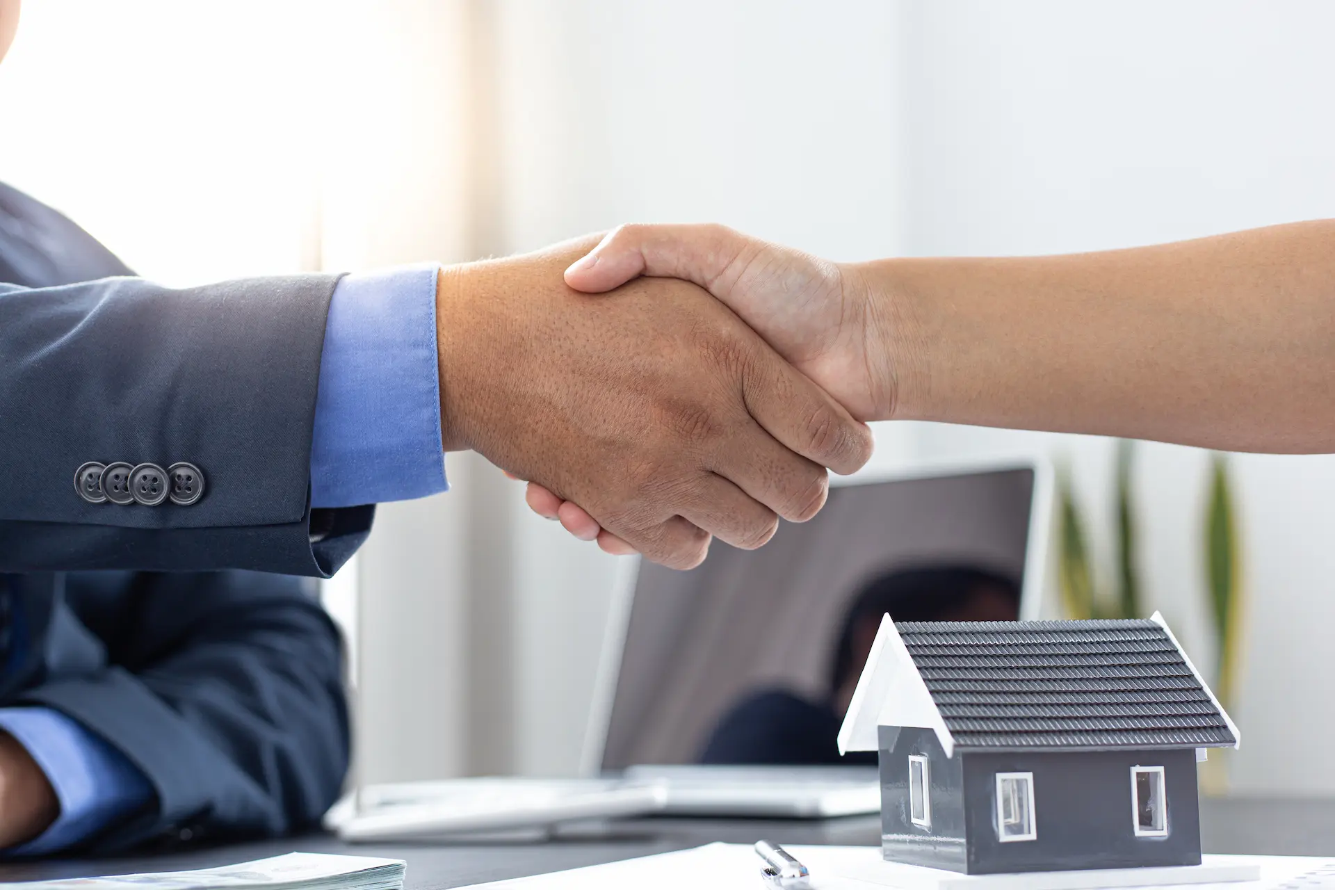 Handshake in front of a house model on a table, symbolizing a real estate deal.
