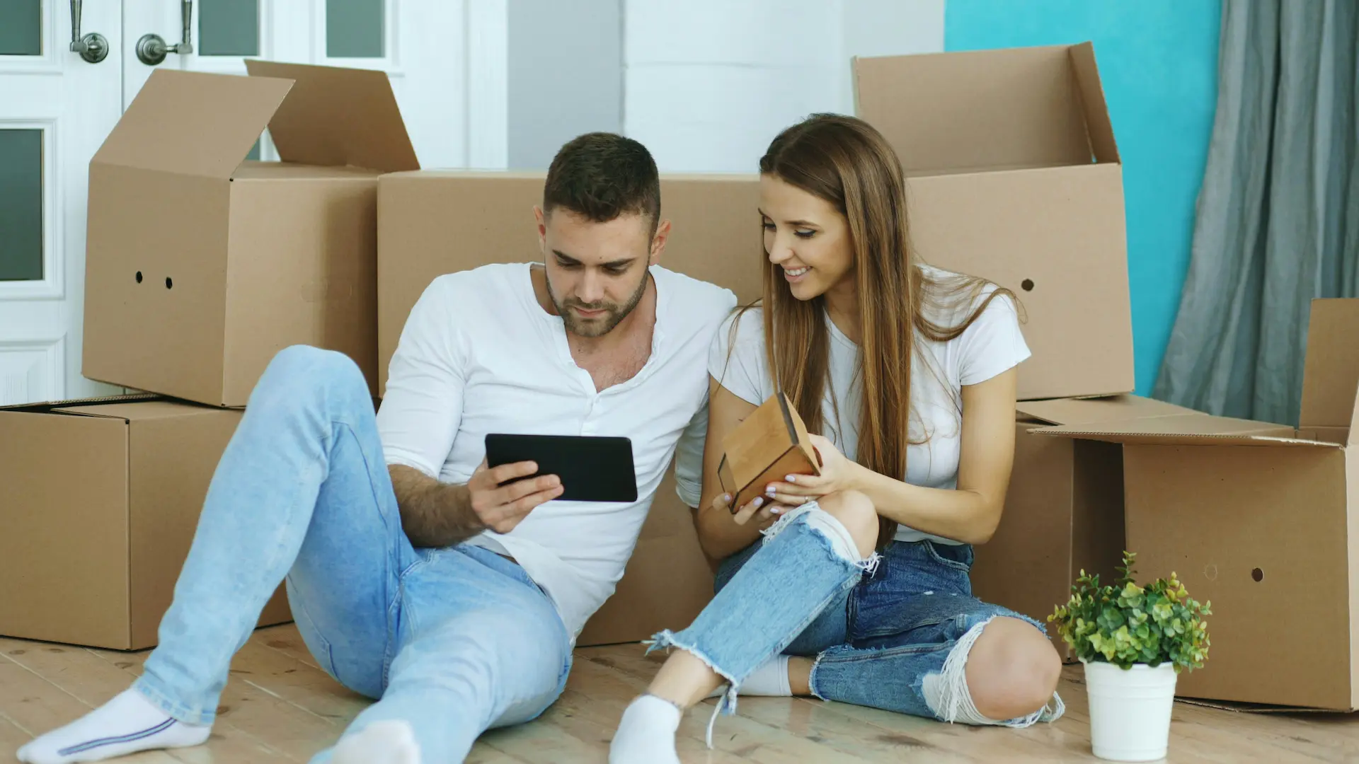 A couple sits among moving boxes and looks at a tablet