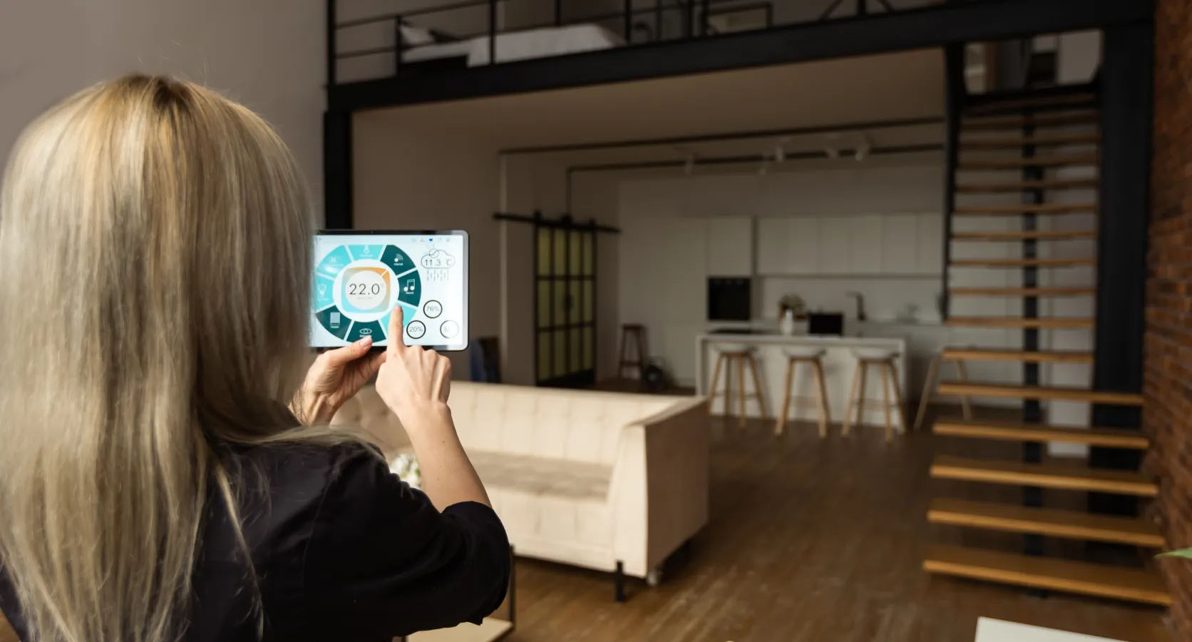 Living trend 2025 – smart home control via tablet in a loft with open kitchen and connected home technology.