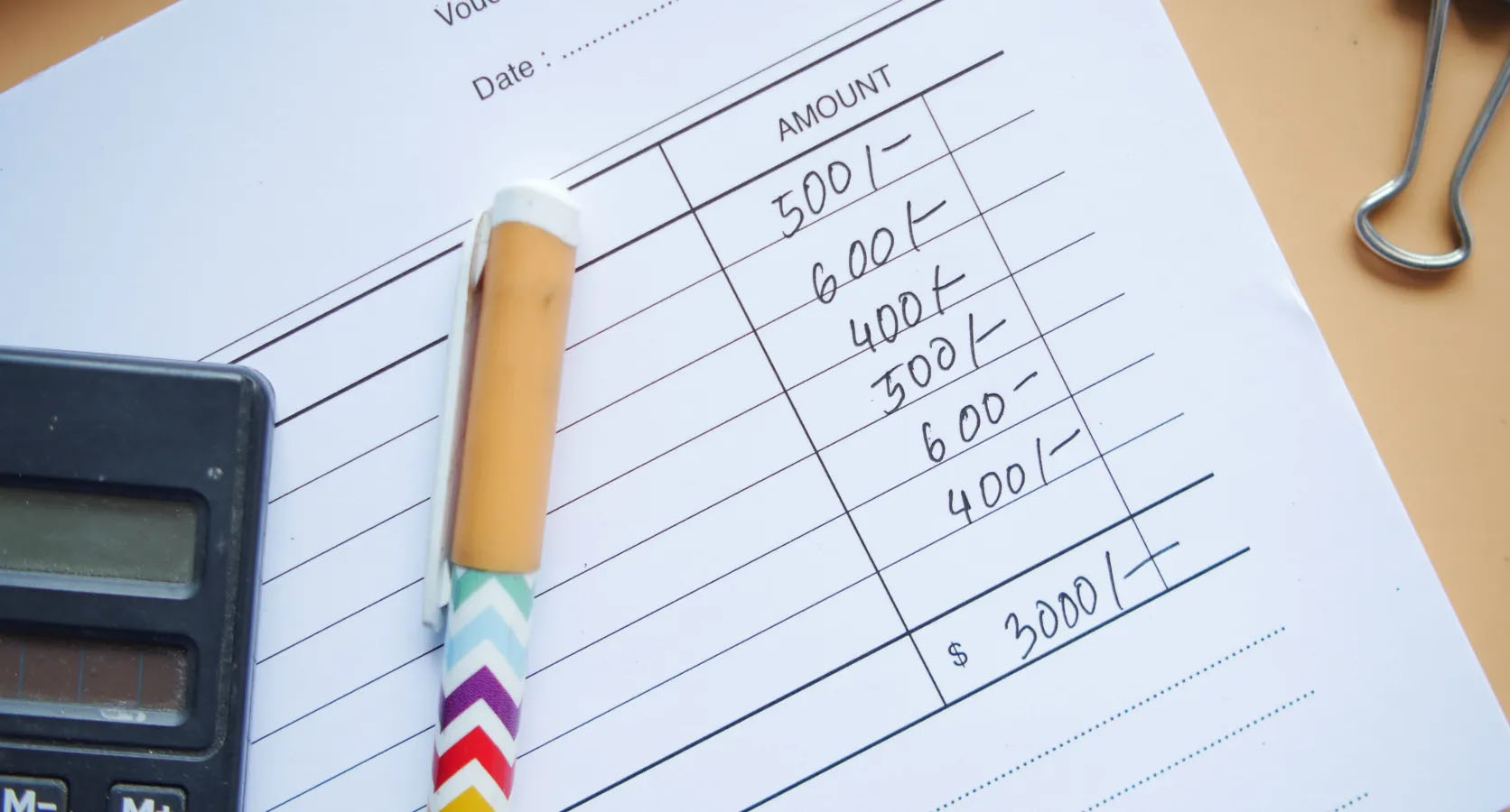 Nahaufnahme eines Vouchers mit handschriftlich notierten Beträgen, daneben ein Taschenrechner und ein bunter Stift – Symbol für Kostenaufstellung oder Finanzplanung.