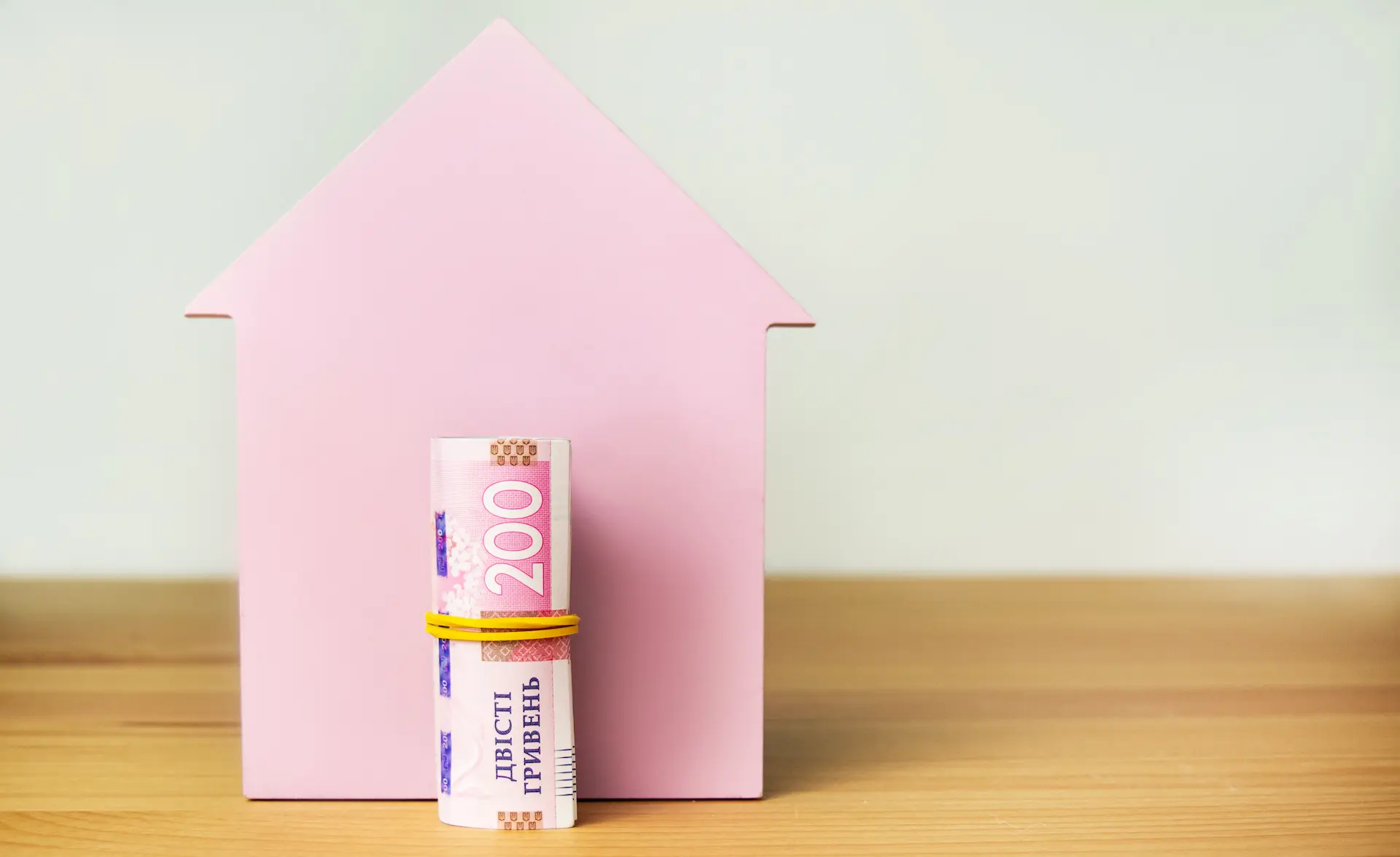 Pink house silhouette with a rolled 200-hryvnia banknote in front.